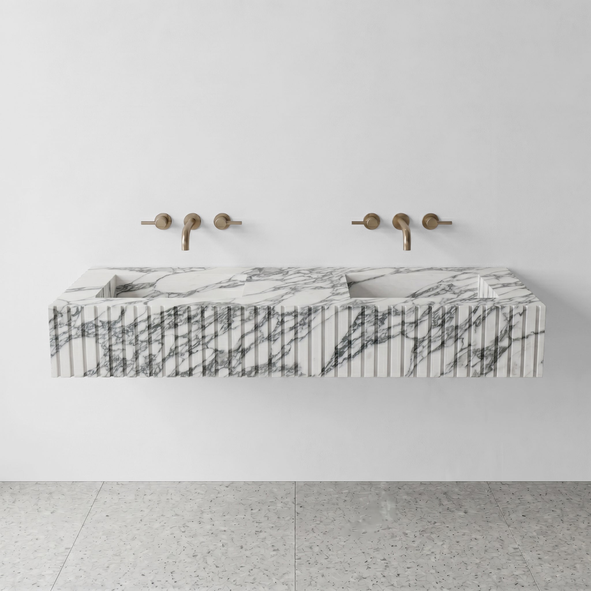 Front profile of a luxury double vanity crafted from Arabescato marble, displaying a custom vertical ribbed apron and brushed gold wall-mounted faucets.