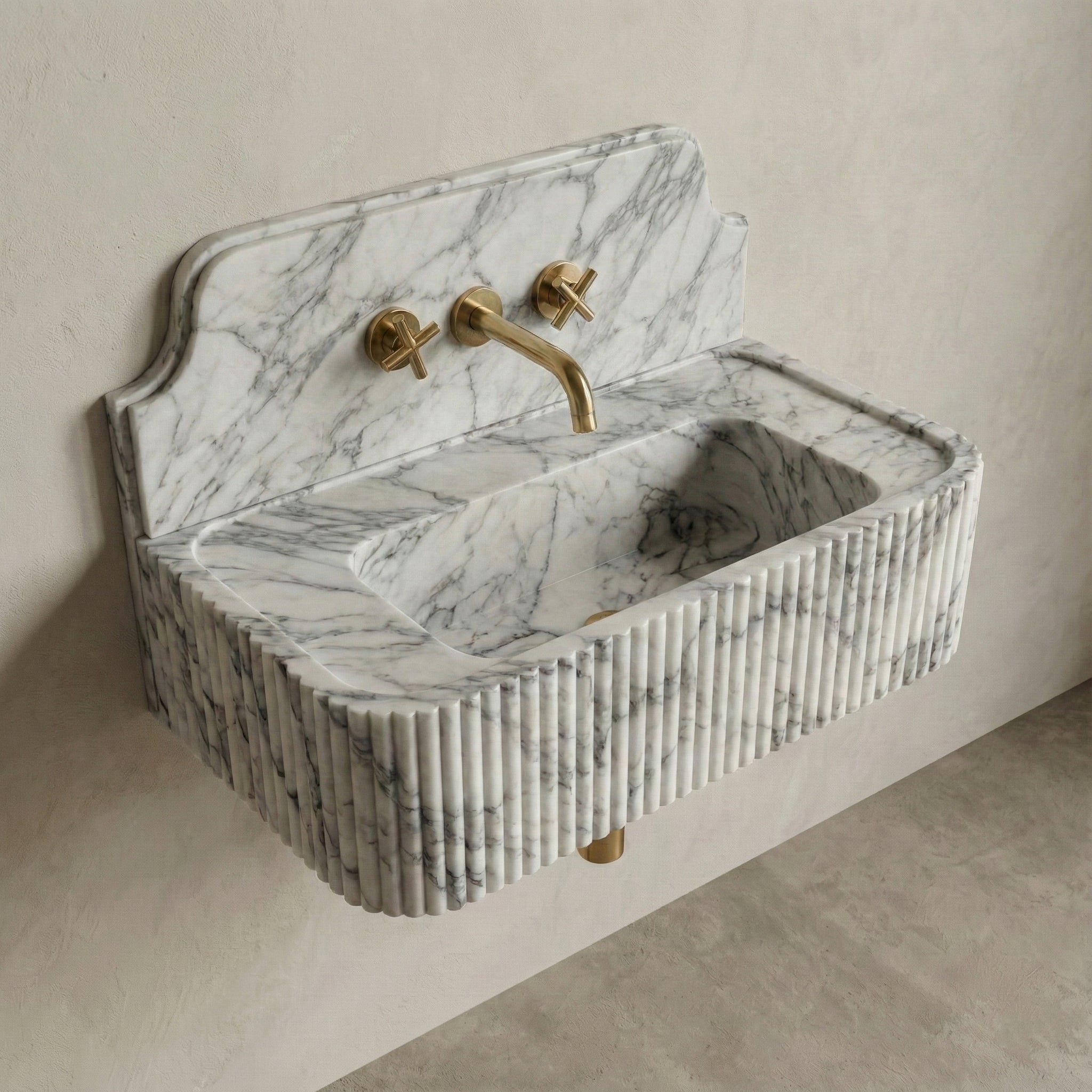 High-angle side view of a vintage-inspired Arabescato marble sink, showcasing the curved stone backsplash, fluted apron detail, and brass cross-handle faucet.