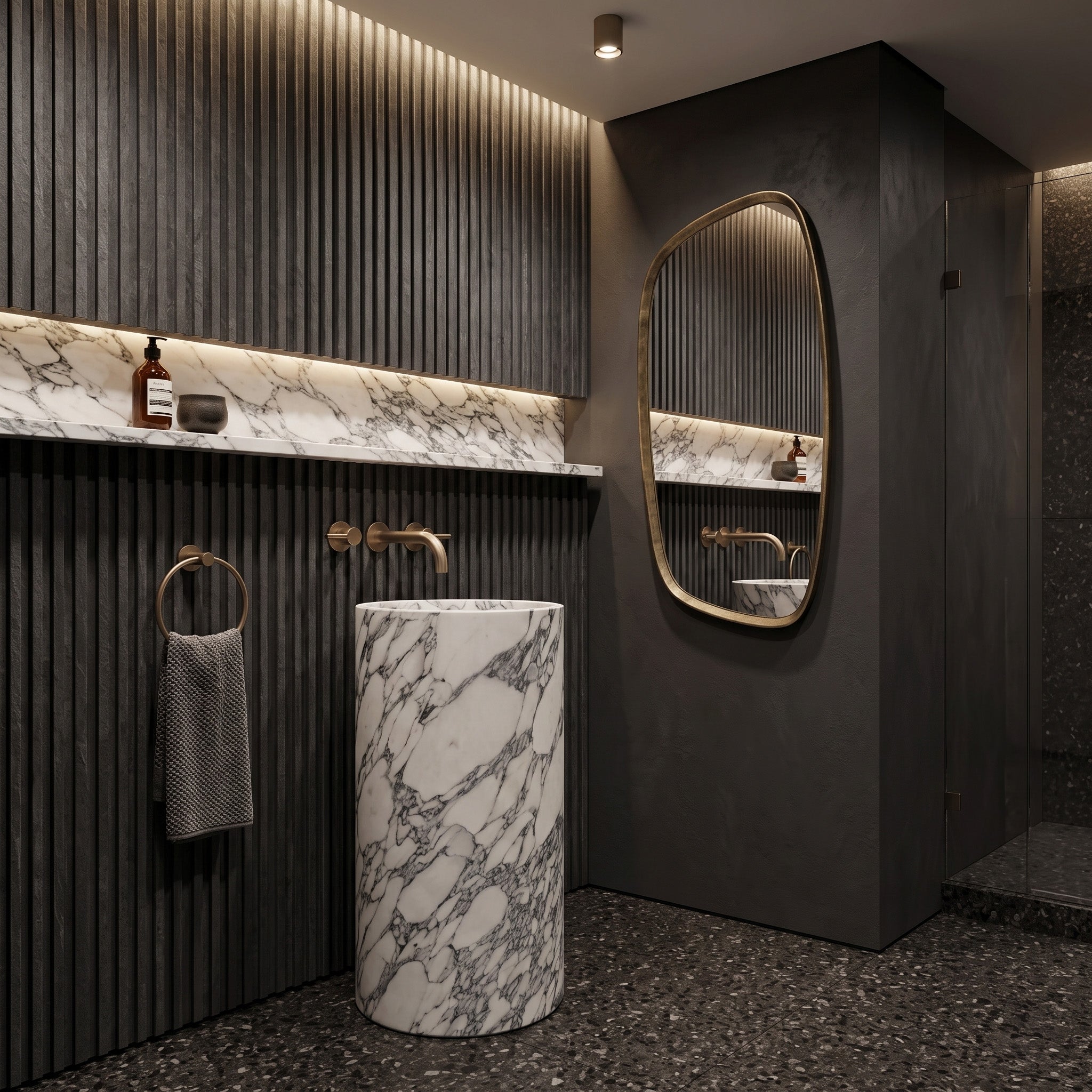 Freestanding Arabescato marble round pedestal basin in a moody luxury bathroom featuring charcoal fluted wall paneling, matching marble shelf, and organic brass mirror.
