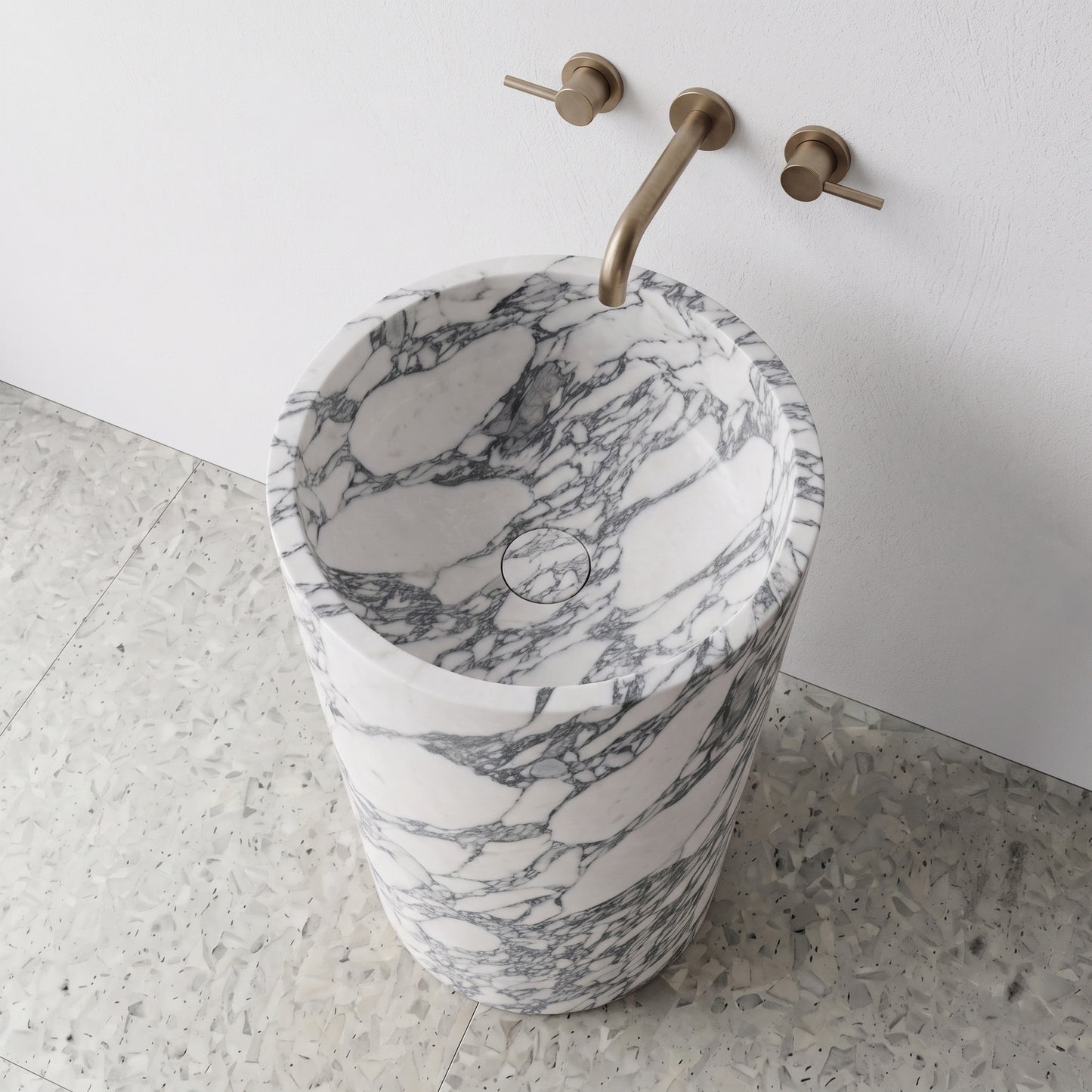 High-angle top view of a solid Arabescato marble cylindrical pedestal sink showing bold grey brecciated veining and matching integrated stone drain cover.