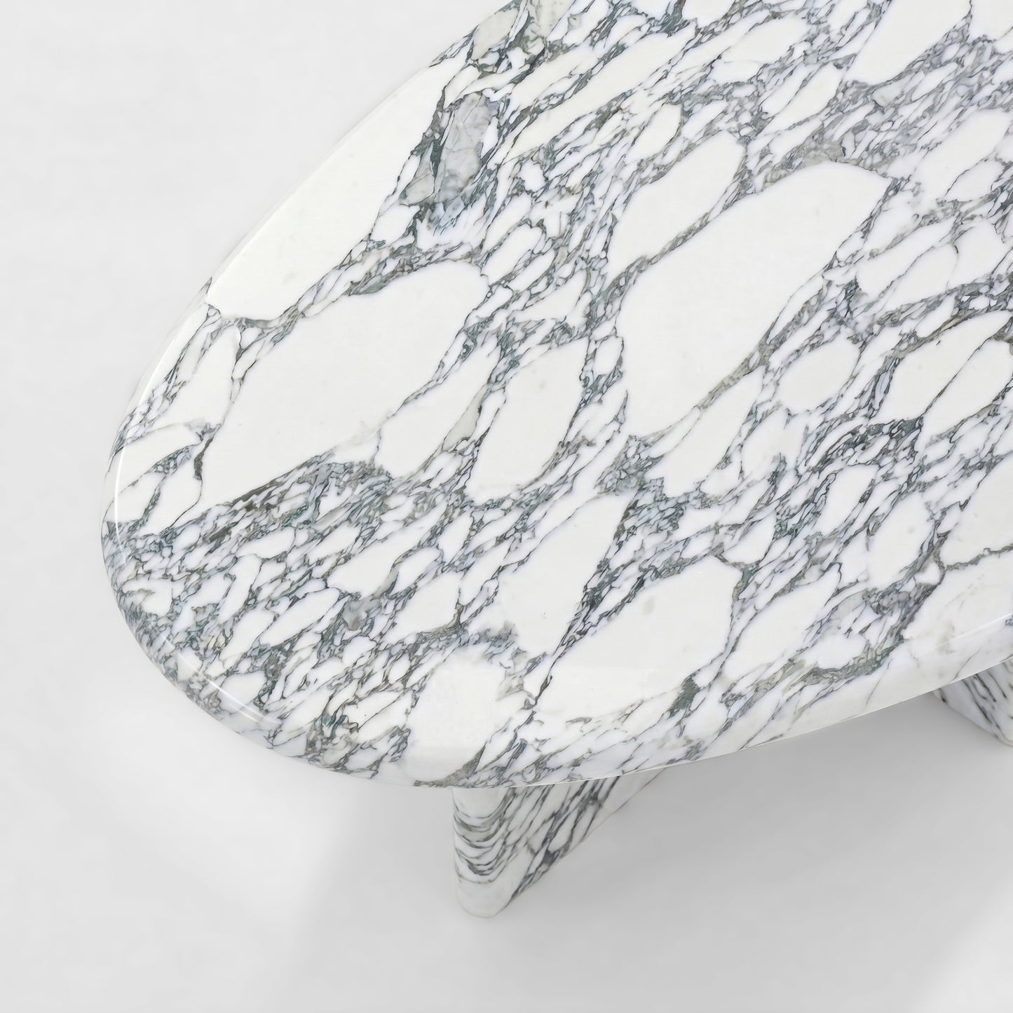 Side profile of a modern Arabescato marble coffee table featuring a thick oval top and a unique sculptural V-shaped pedestal base against a minimalist white background.