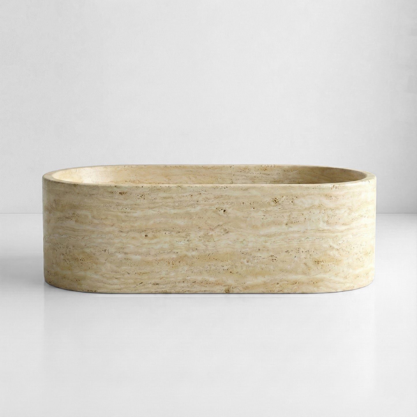 Front view of a solid oval bathtub carved from beige travertine, featuring horizontal limestone veining and a honed finish.