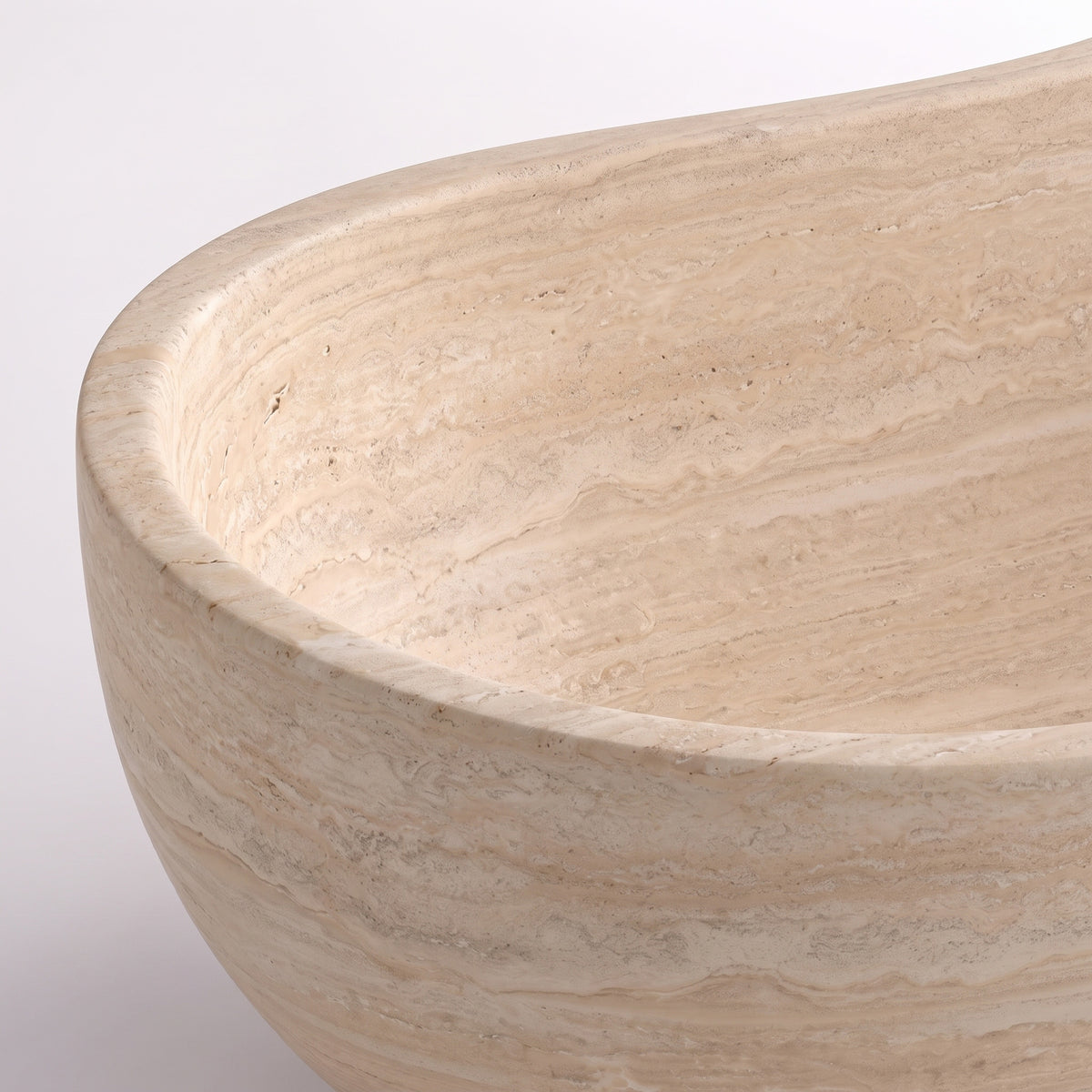 Close-up overhead detail shot of the Beige Travertine wave bathtub rim, displaying the smooth hand-finished curve, subtle natural stone porosity, and layered cream-and-sand sedimentary grain.