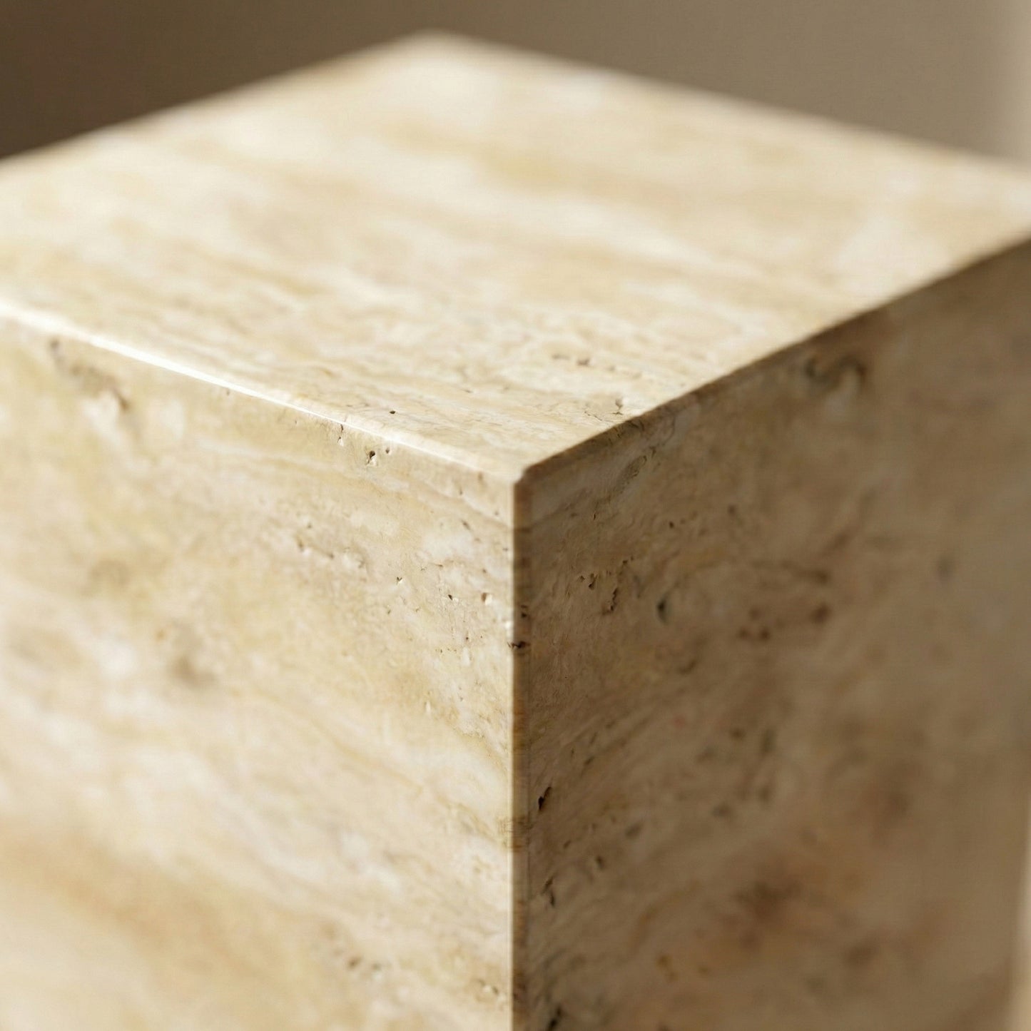A detailed close-up of the corner of a Beige Travertine pedestal, highlighting the natural pitted texture, honey-colored sediment layers, and the seamless mitered joint.