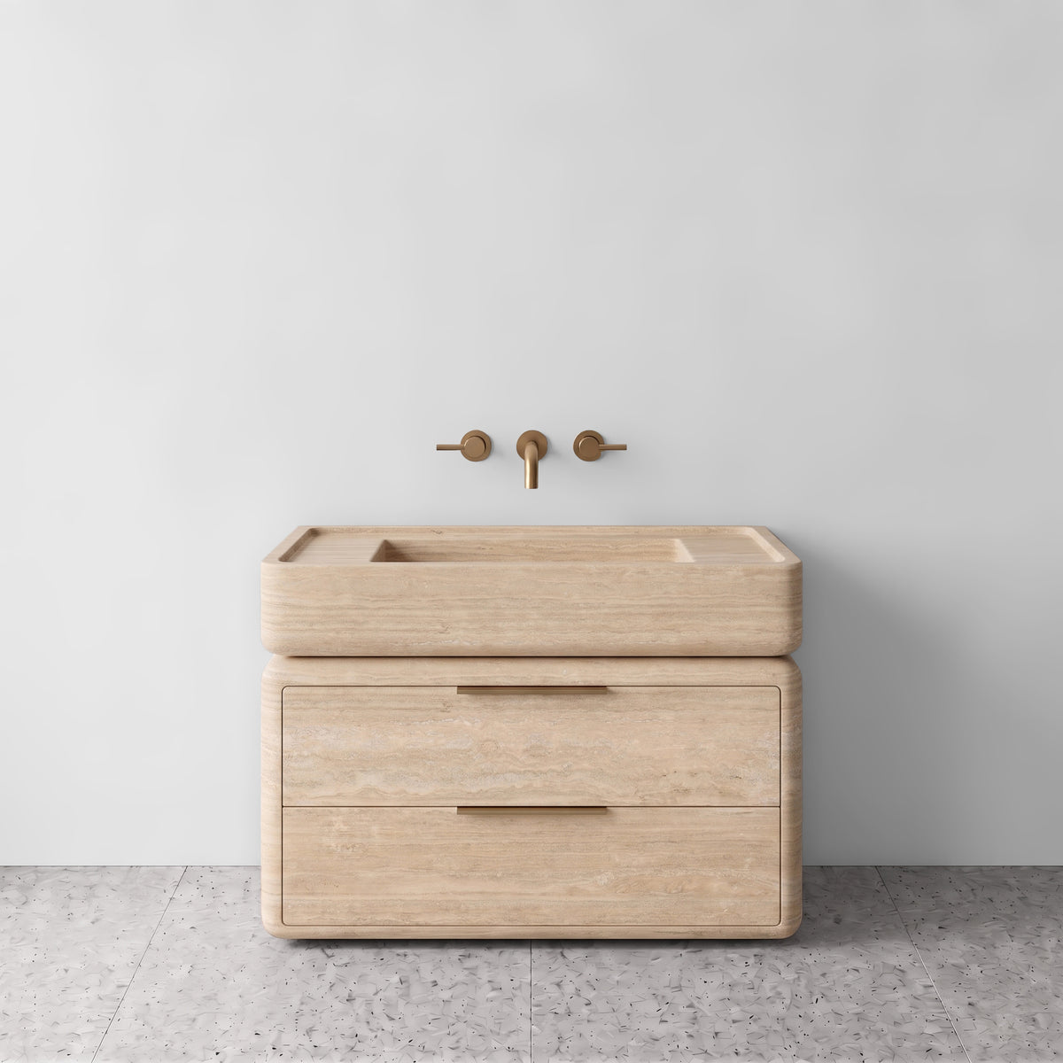 Front studio view of the freestanding Beige Travertine double-drawer vanity, featuring soft rounded corners, an integrated trough basin, horizontal brushed brass pulls, and wall-mounted three-hole brass tapware set against a neutral wall and terrazzo flooring.