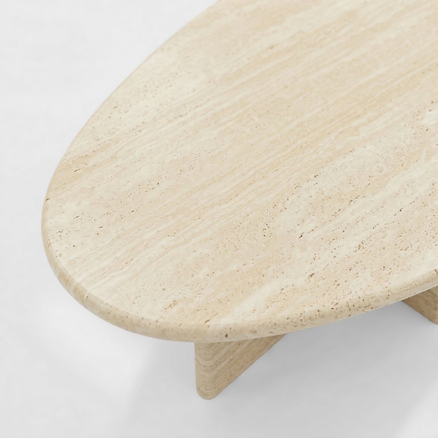 Side profile of a bespoke beige travertine coffee table featuring a sculptural V-shaped pedestal base and an organic pebble-shaped top.