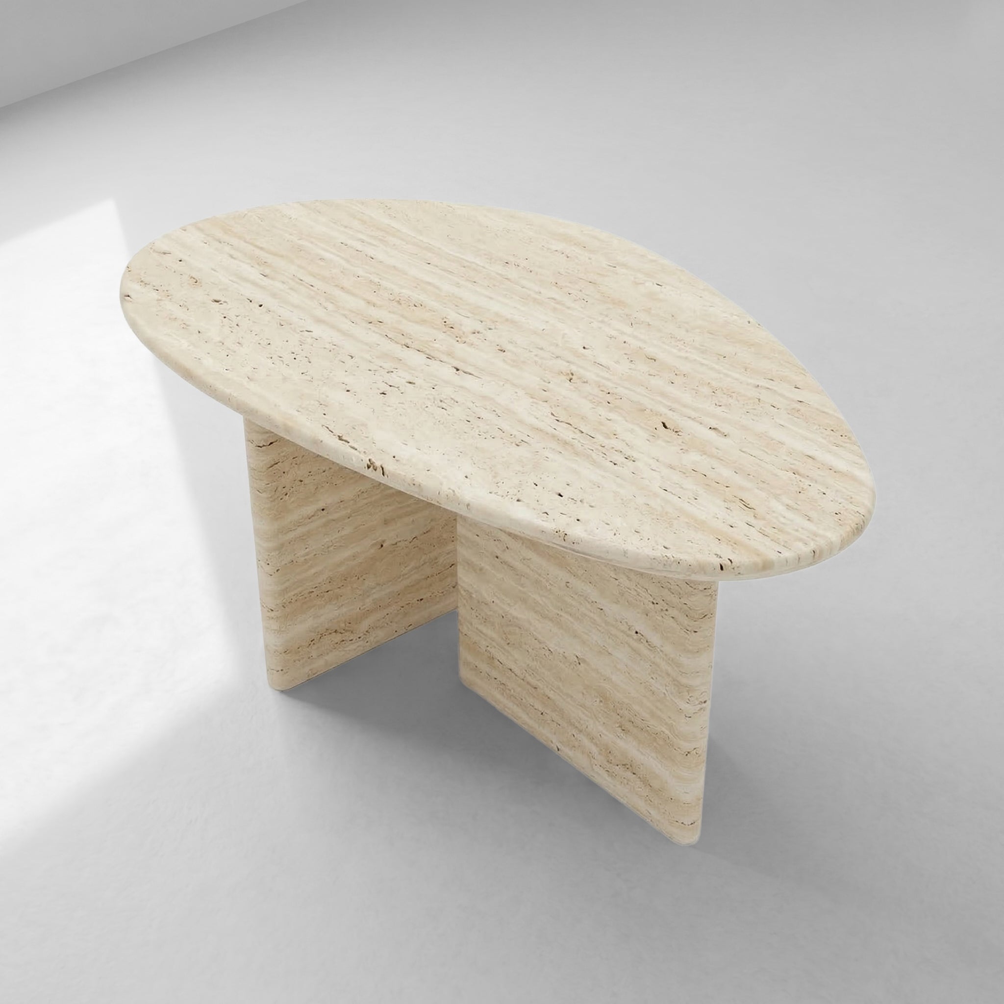 High-angle view of a pebble-shaped beige travertine coffee table showcasing its unique organic silhouette and minimalist two-pedestal design.
