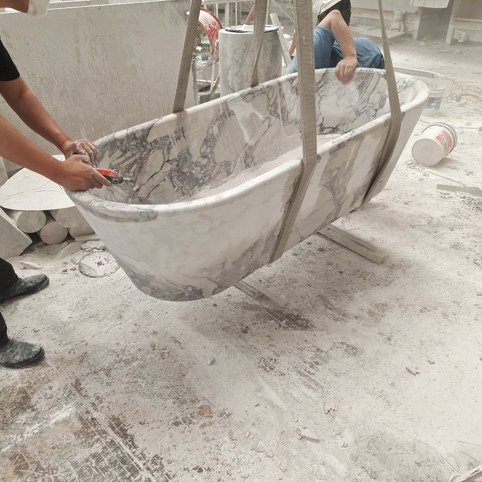 Factory production shot showing the careful handling and lifting of a custom Calacatta Viola marble bathtub during the manufacturing process.