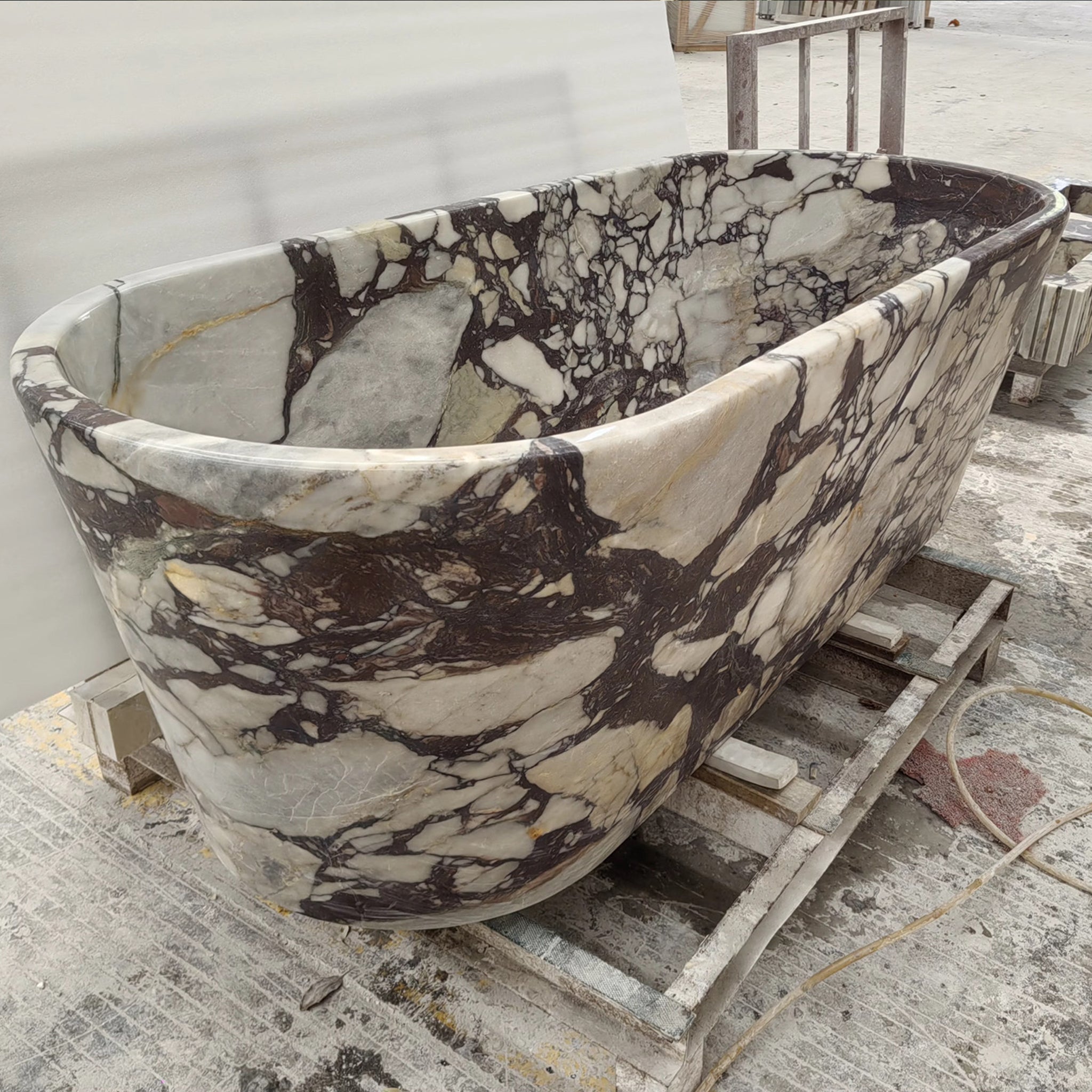 Side profile of a handcrafted Calacatta Viola marble bathtub resting on a pallet, displaying the unique purple and white mineral patterns.