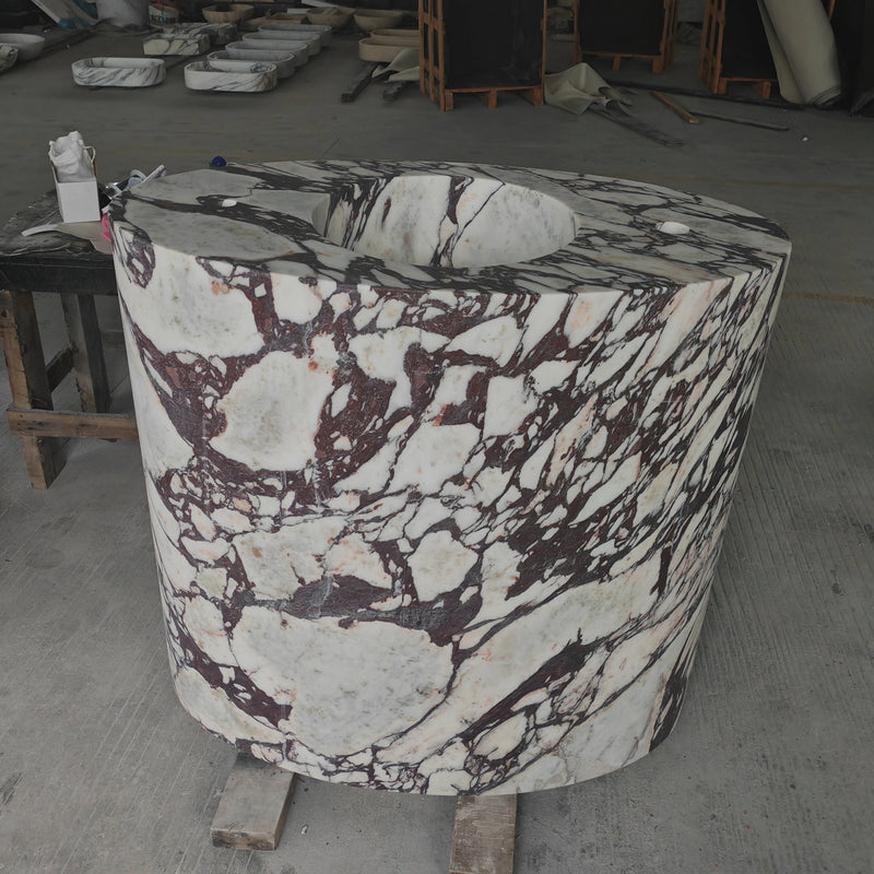 Solid block freestanding cylindrical washbasin carved from Calacatta Viola marble with dramatic purple veining.