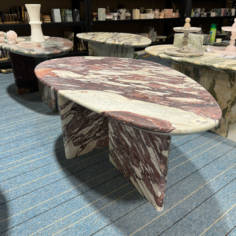 An elegant oval Calacatta Viola coffee table with a cross-base design, displayed alongside other bespoke natural stone tables in the GustavDesign furniture showroom.