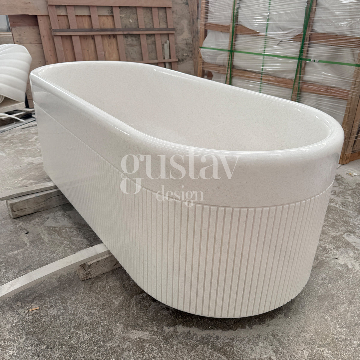 Freestanding Crystal White marble bathtub featuring a modern fluted texture and a polished rim, shown inside a stone carving warehouse by GustavDesign.