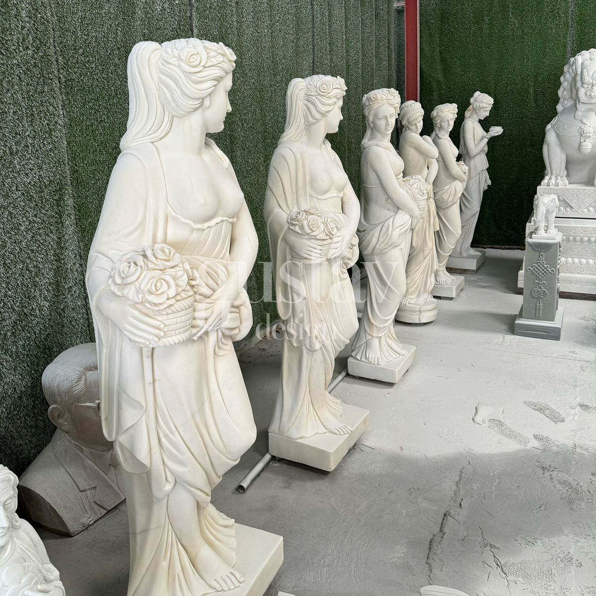 A row of classically inspired white marble female statues, hand-carved with intricate floral and drapery details for luxury garden and interior decor by GustavDesign.