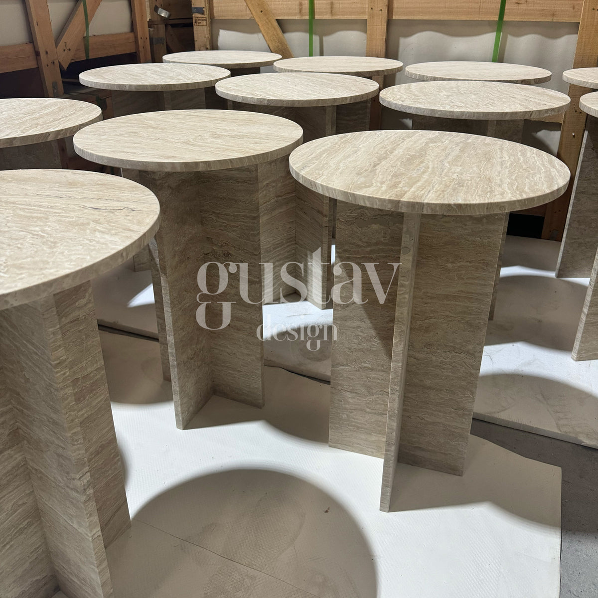 A series of bespoke beige travertine side tables with architectural cross-bases, ready for delivery as part of a luxury stone furniture commission by GustavDesign.