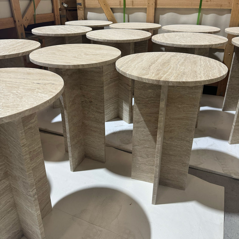 A series of bespoke beige travertine side tables with architectural cross-bases, ready for delivery as part of a luxury stone furniture commission by GustavDesign.