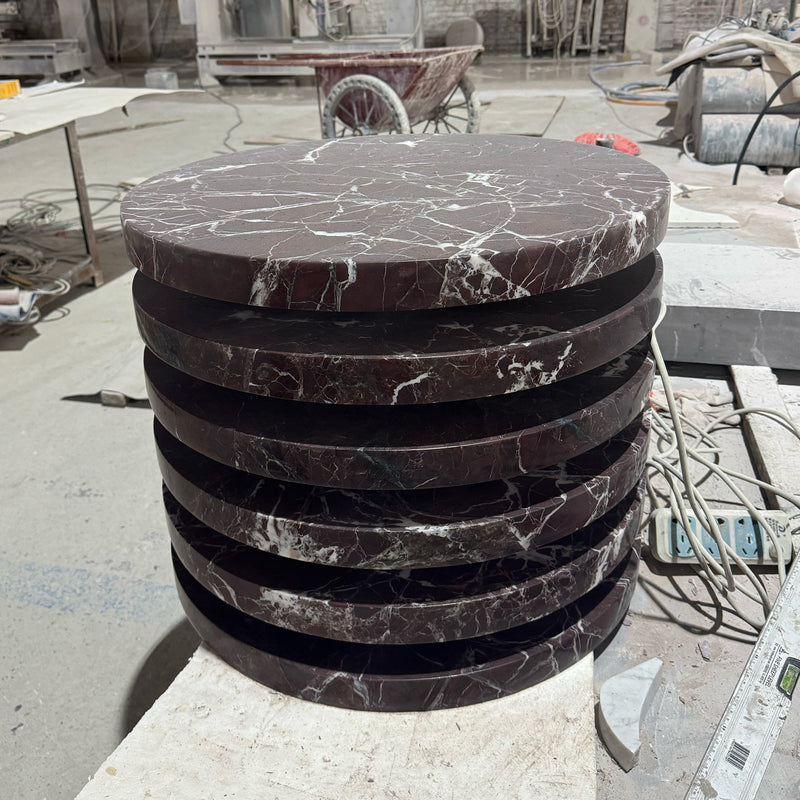 Precision-cut Rosso Levanto marble circular table tops stacked for assembly in the GustavDesign stone fabrication facility, intended for bespoke dining furniture.