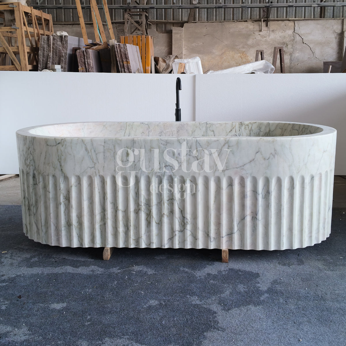 Freestanding Calacatta Green marble bathtub with a scalloped fluted exterior, positioned with a black faucet mock-up inside a stone workshop by GustavDesign.