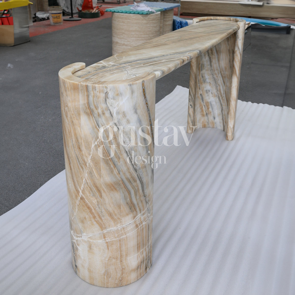 Elegant curved onyx console table with dramatic tan, grey, and cream natural veining, luxury stone entryway furniture by Gustav Design.