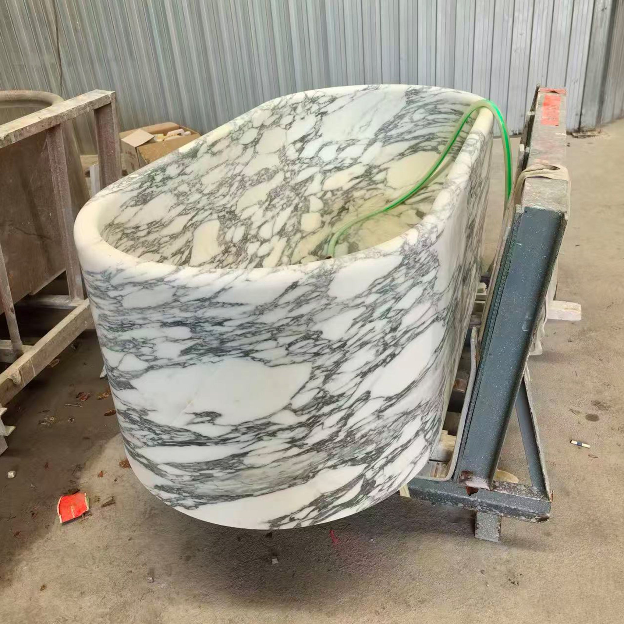 Manufacturing phase of a custom white Arabescato marble bathtub mounted on a steel frame for final surface finishing.