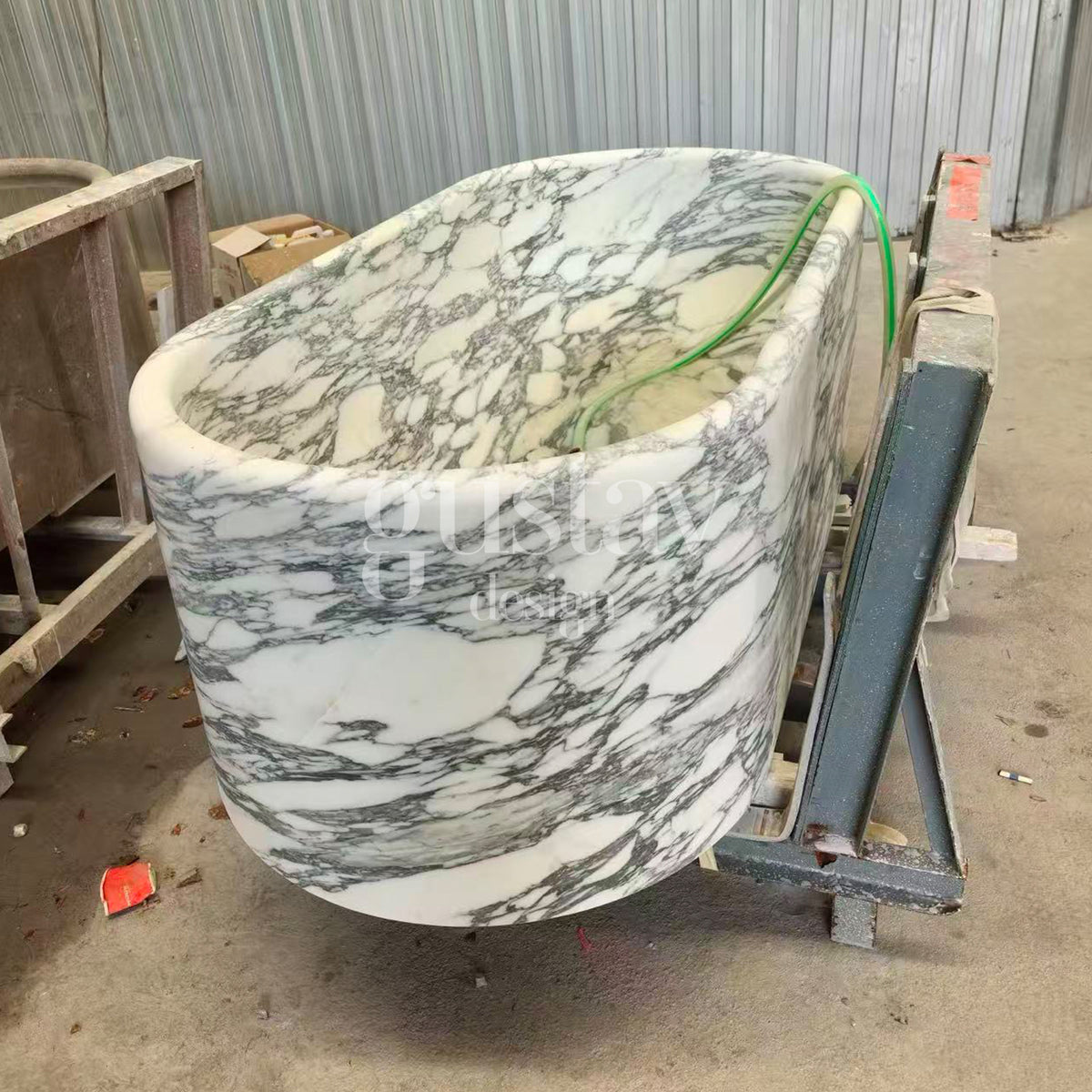 Manufacturing phase of a custom white Arabescato marble bathtub mounted on a steel frame for final surface finishing.