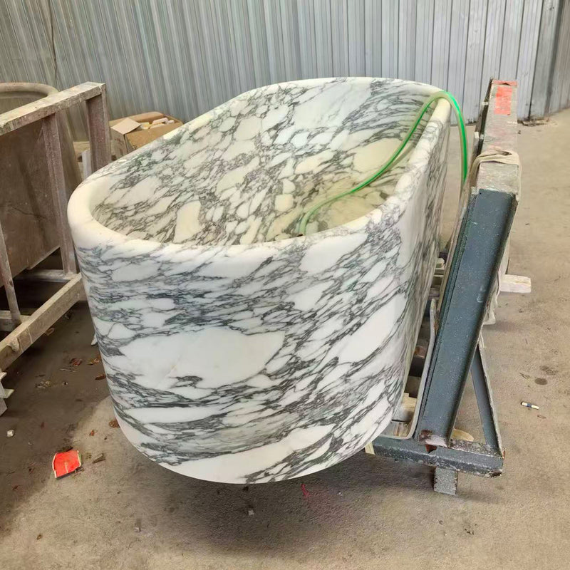 Manufacturing phase of a custom white Arabescato marble bathtub mounted on a steel frame for final surface finishing.