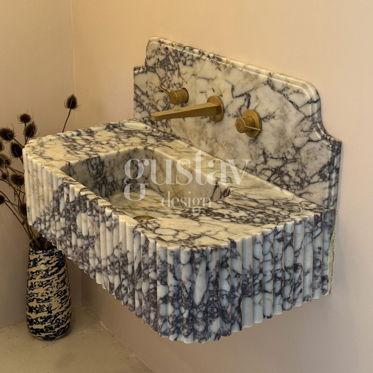 Floating Calacatta Viola marble sink featuring a continuous vertical fluted apron, shaped stepped backsplash, and wall-mounted brass tapware