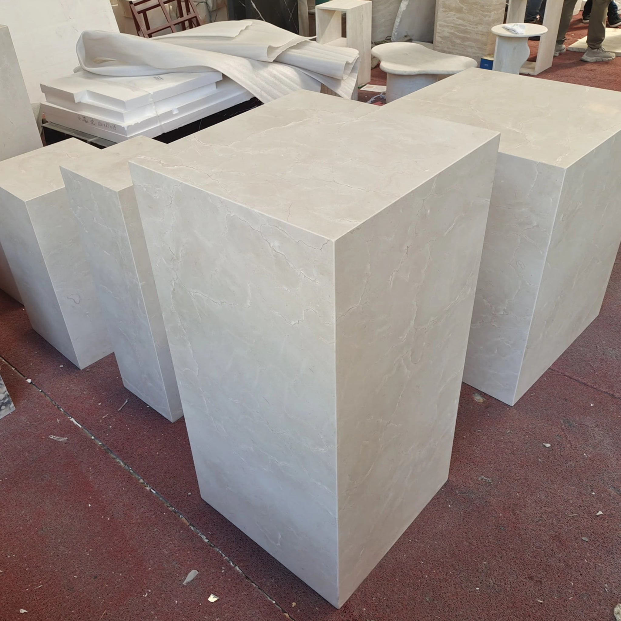 Set of custom-fabricated beige limestone display plinths and cubic pedestals awaiting final inspection in the stone workshop.