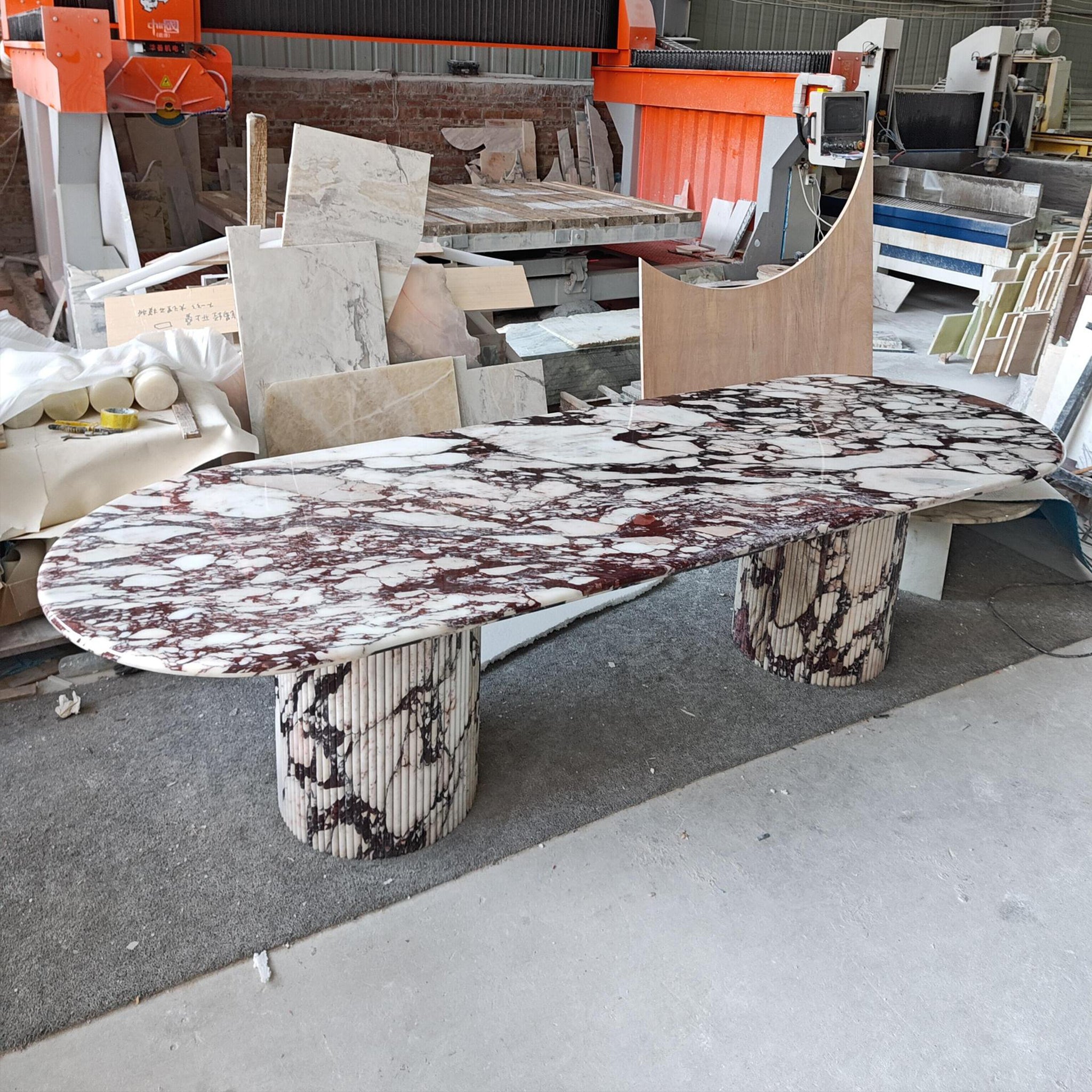 Large custom-made oval dining table featuring a Calacatta Viola marble top and matching fluted cylindrical stone bases.