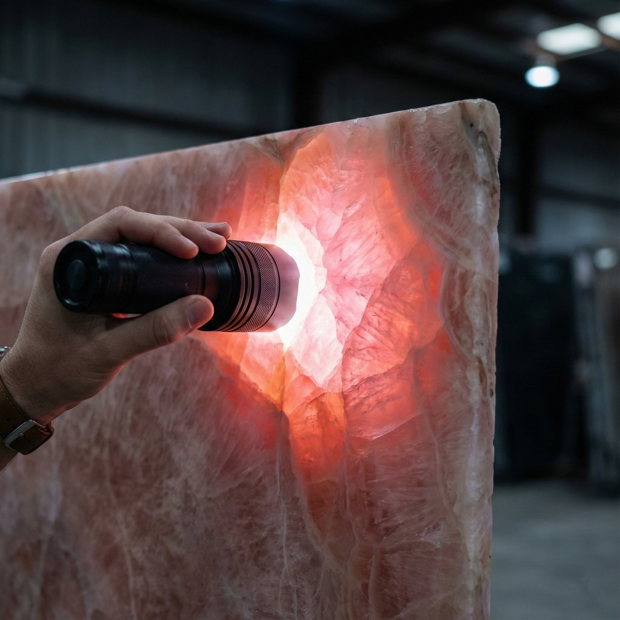Quality control inspection of a translucent Pink Onyx slab, using a flashlight to reveal the stone's internal crystalline structure and color depth.