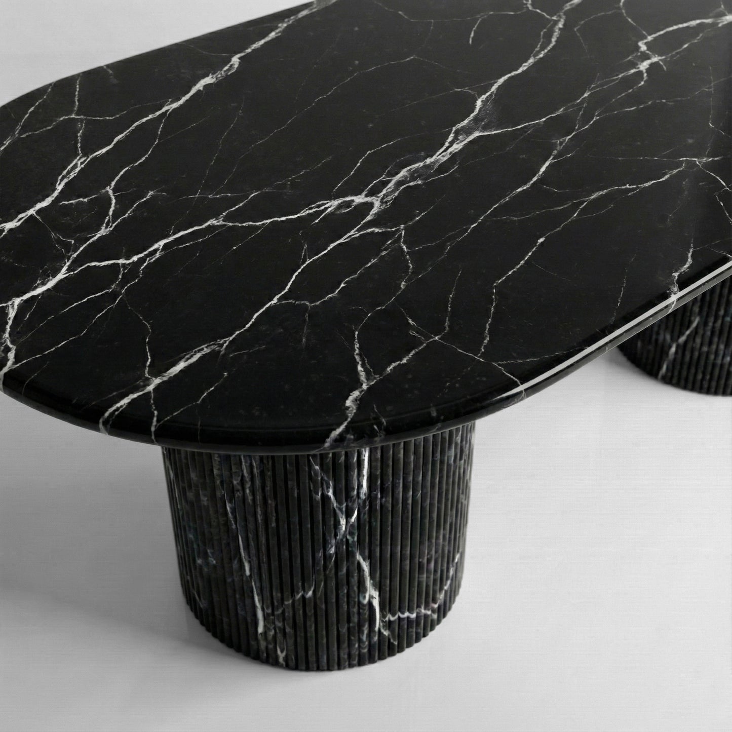 Close-up side profile of a Black Marquina marble dining table showing the sleek beveled edge and matching ribbed pedestal legs in deep charcoal stone.