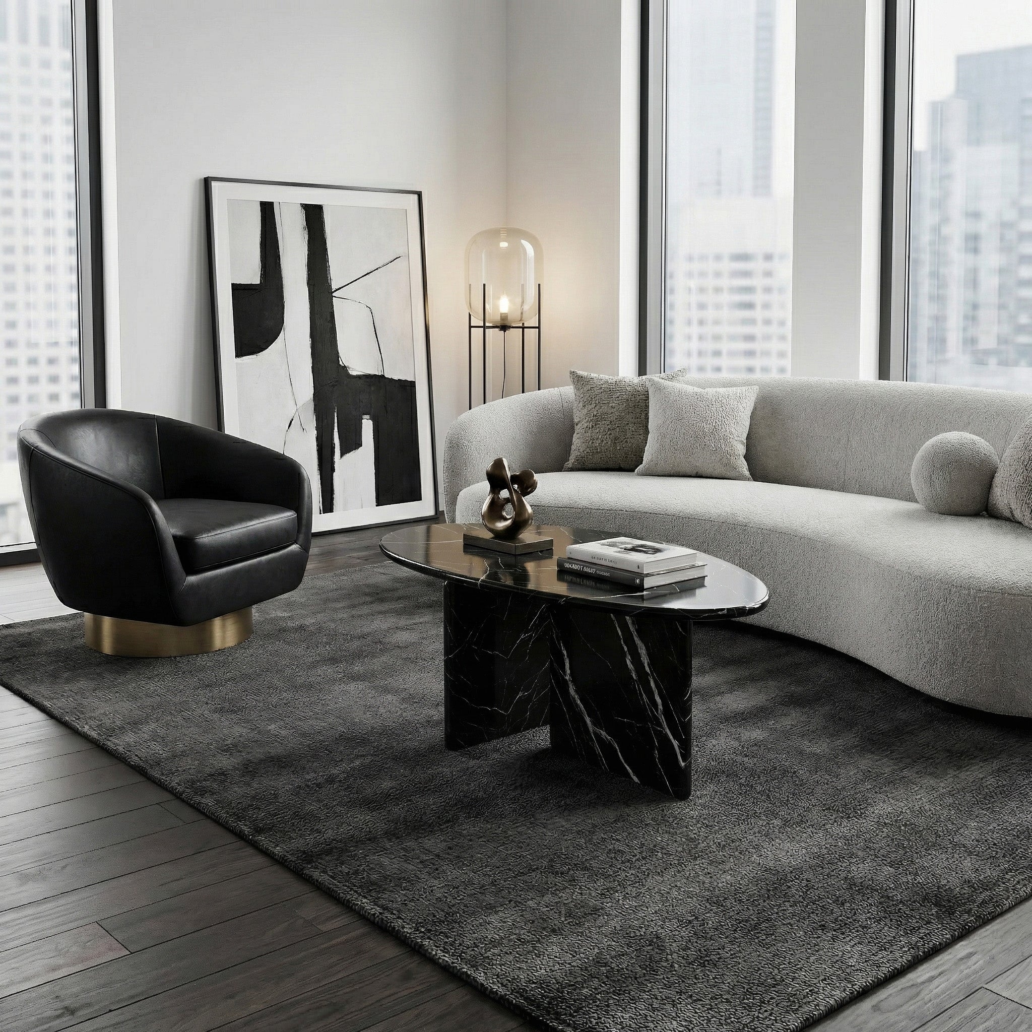 Modern high-rise living room featuring an oval Black Marquina marble coffee table styled on a plush grey rug with a curved sofa and a black leather accent chair.