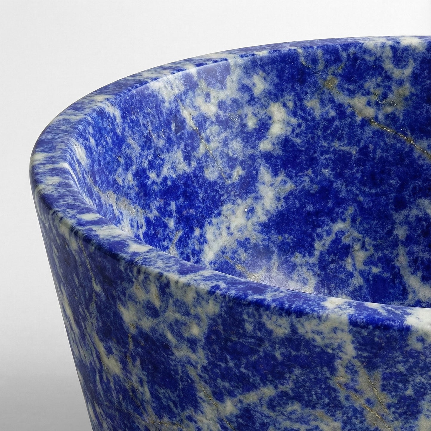 Close-up detail of a Blue Sodalite bathtub rim highlighting the vibrant ultramarine color and sparkling metallic gold inclusions natural to the gemstone.