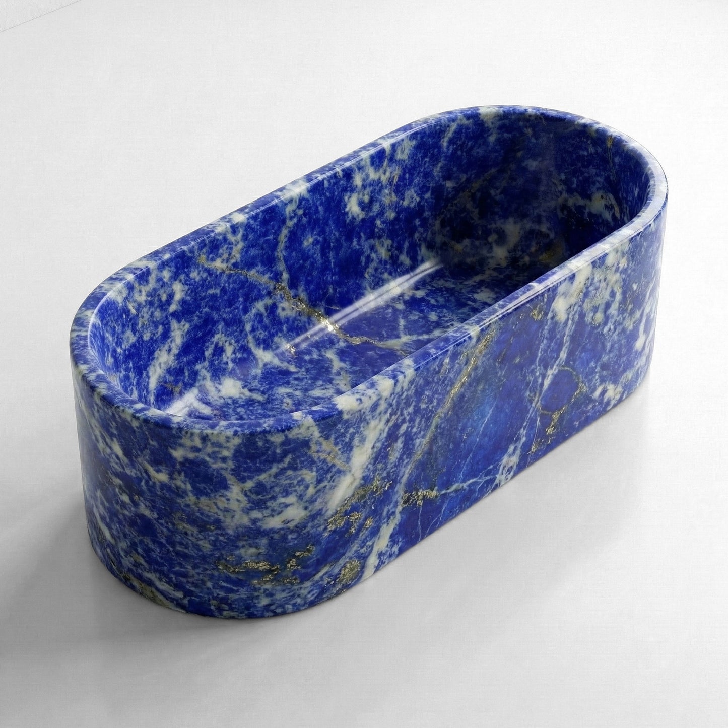 Isometric side view of a semi-precious Blue Sodalite bathtub showing the deep royal blue surface speckled with natural gold pyrite flecks.