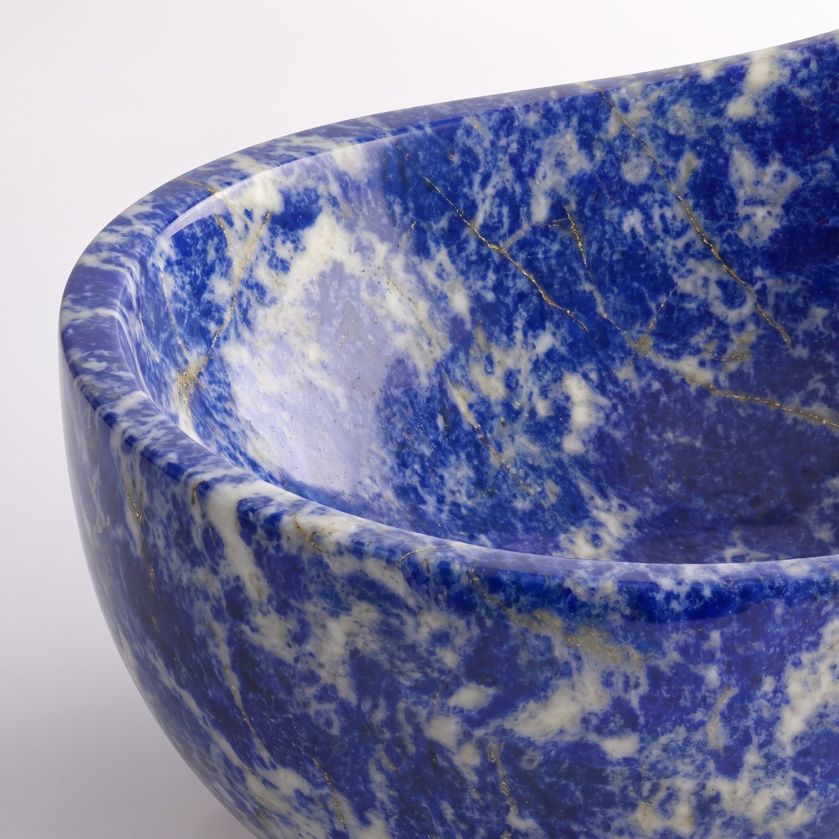 Close-up overhead detail shot of the Blue Sodalite marble wave bathtub rim, displaying the hand-finished curve, polished stone texture, and vivid royal blue mineral field accented by delicate golden veining and white calcite.