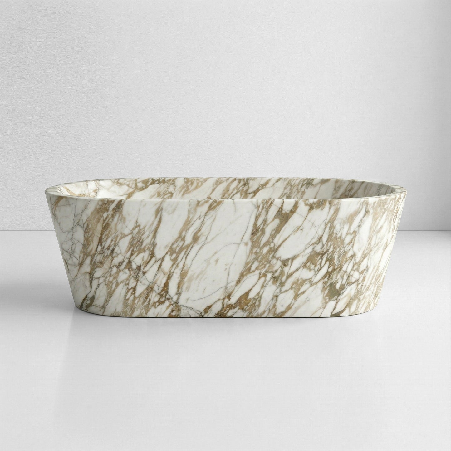 A front-facing view of a freestanding, tapered marble bathtub made from white Calacatta Gold marble with dramatic, heavy grey and gold veining.
