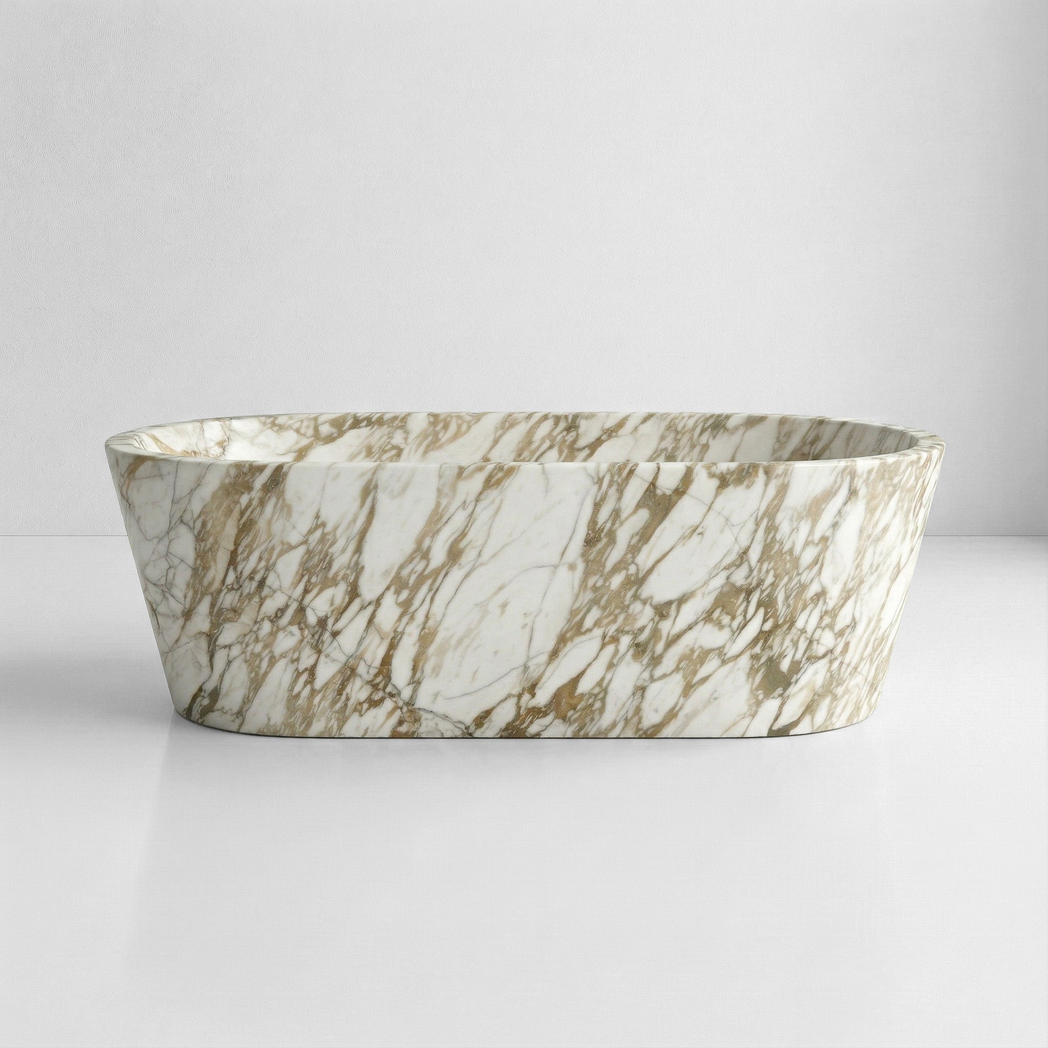 A front-facing view of a freestanding, tapered marble bathtub made from white Calacatta Gold marble with dramatic, heavy grey and gold veining.