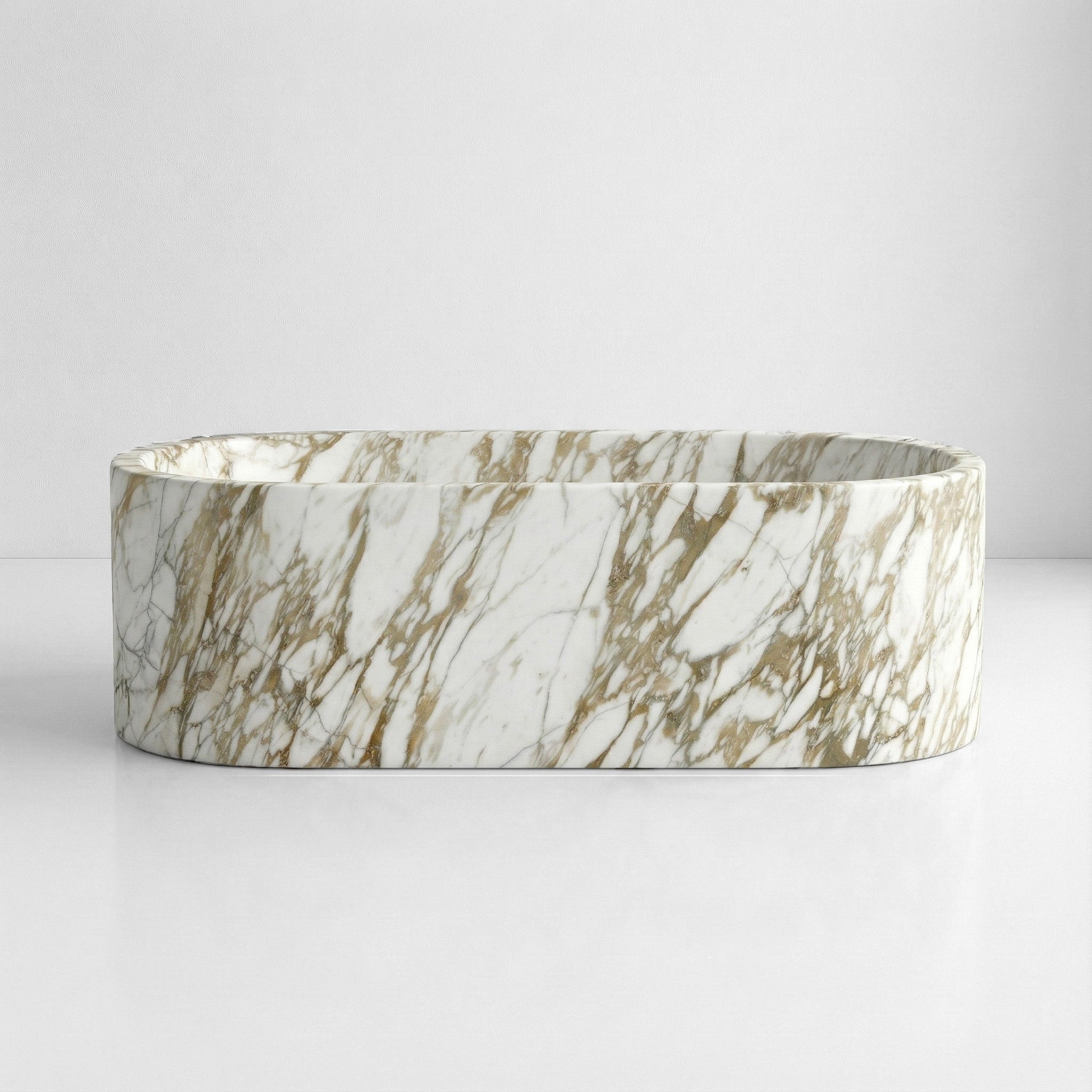A front view of a freestanding oval Calacatta Gold bathtub with vertical, straight sides, carved from white marble with dense gold and charcoal veining.