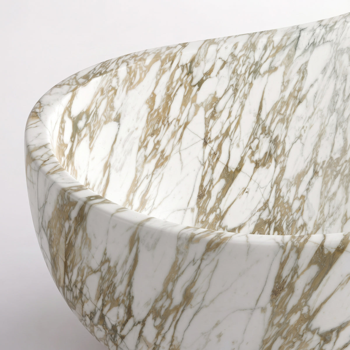 Close-up overhead detail shot of the Calacatta Gold marble wave bathtub rim, displaying the hand-finished curve, polished stone texture, and delicate golden ribbons traversing crystalline white marble.