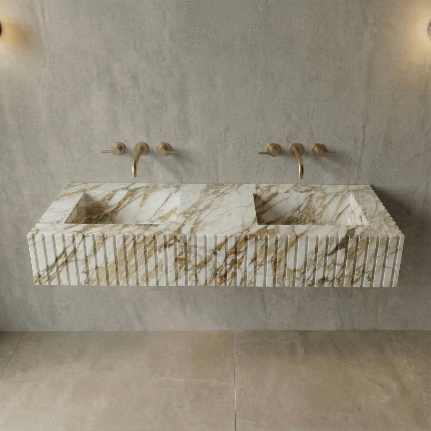 A front view of a wall-mounted double vanity sink made from Calacatta Gold marble. The front face features a vertical fluted (ribbed) texture, paired with minimalist brushed gold wall-mounted faucets.