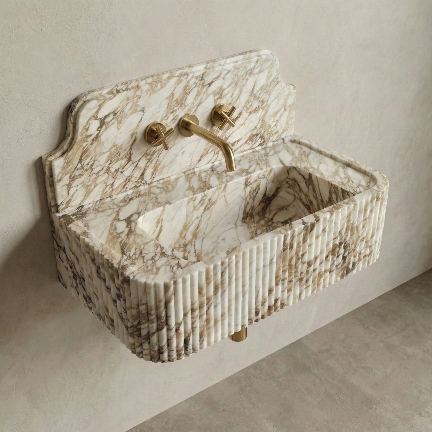 High-angle side view of a vintage-inspired Calacatta Gold stone sink, highlighting the curved backsplash silhouette, fluted apron detail, and brass wall-mounted faucet.