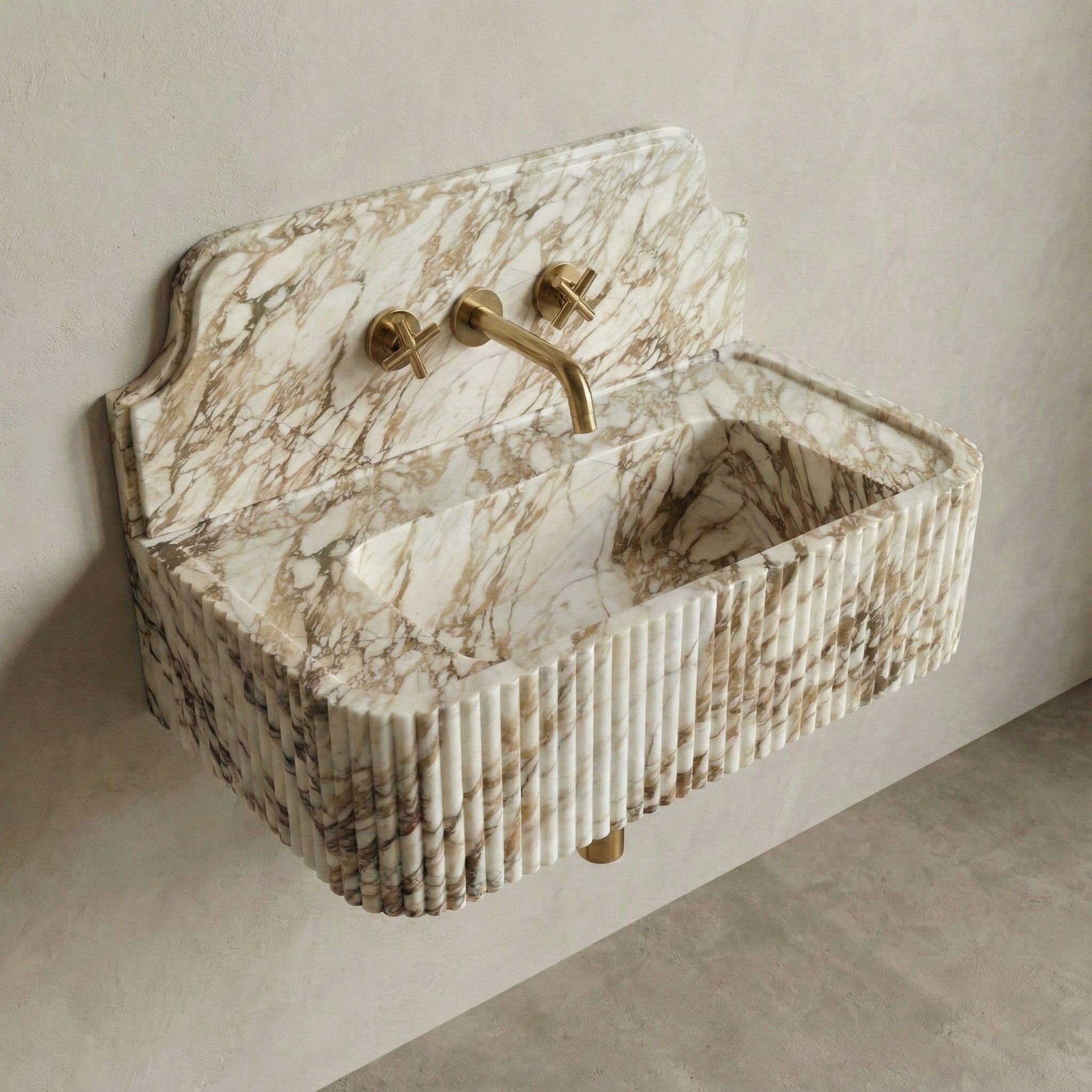 High-angle side view of a vintage-inspired Calacatta Gold stone sink, highlighting the curved backsplash silhouette, fluted apron detail, and brass wall-mounted faucet.