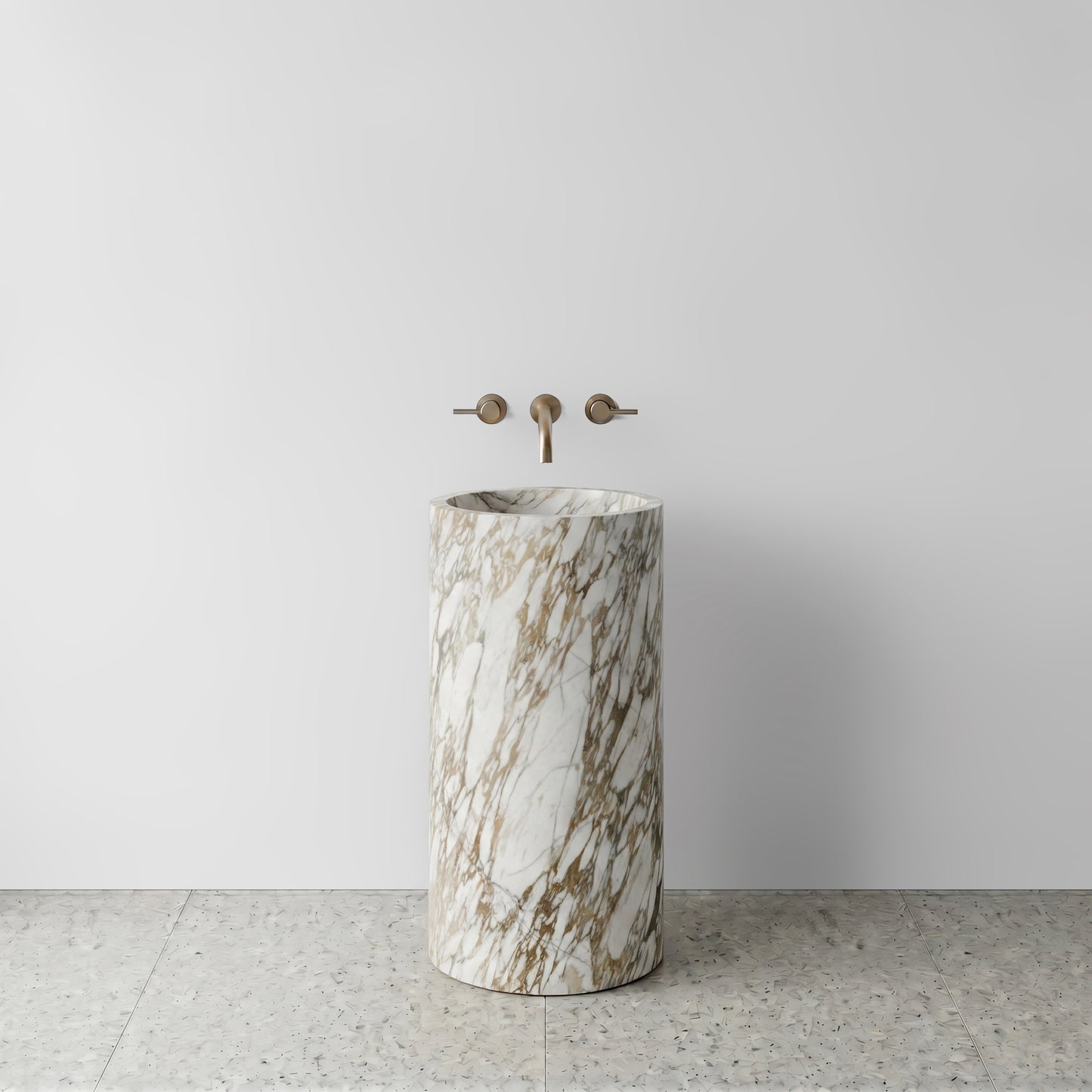 Front view of a solid Calacatta Gold marble cylinder pedestal sink on light terrazzo flooring with wall-mounted brushed bronze faucet.