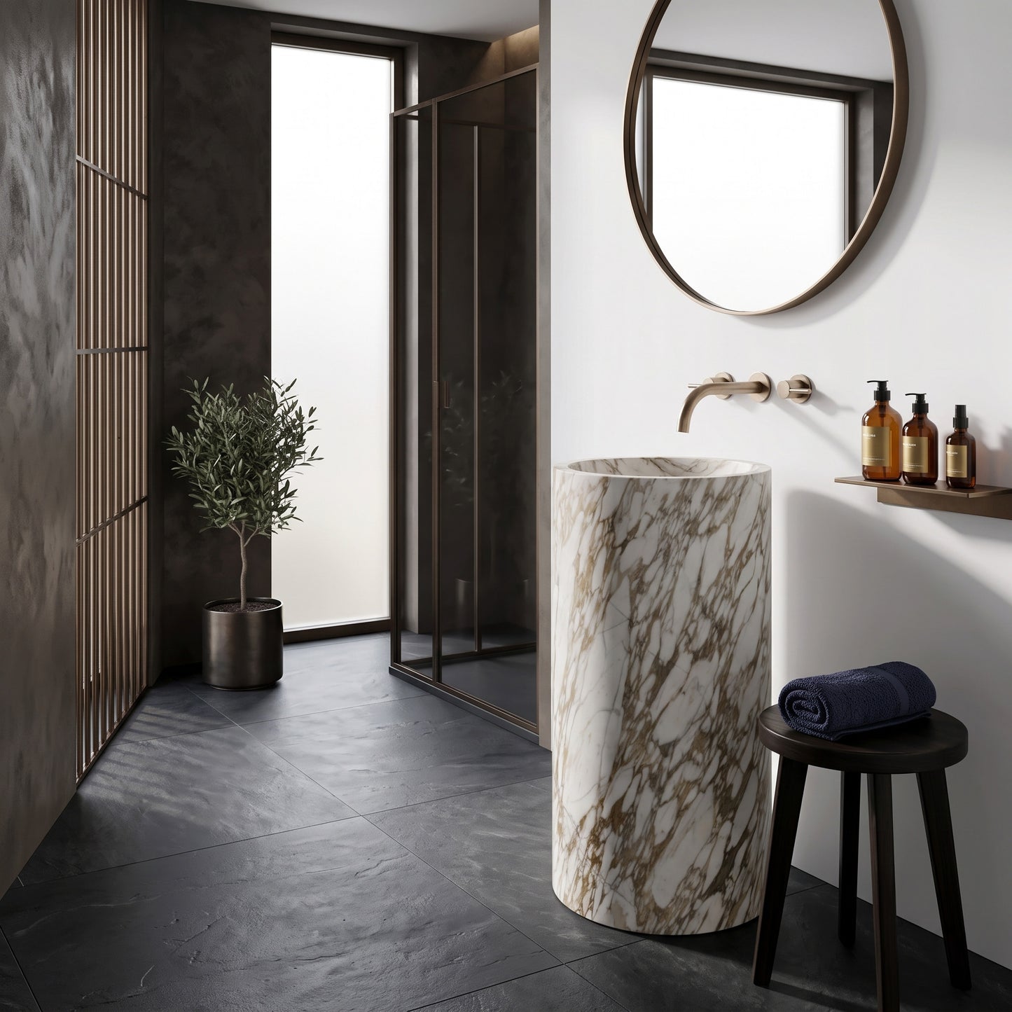 Freestanding Calacatta Gold marble round pedestal basin in a modern luxury bathroom featuring charcoal slate floors, round mirror, and potted olive tree.