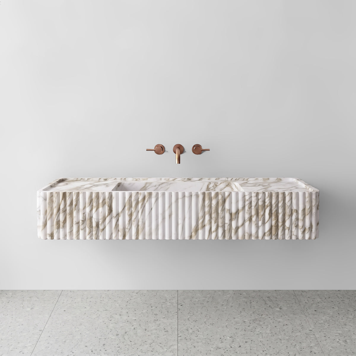 Front view of the Calacatta Gold marble fluted monolith sink showing warm honey-gold and grey veining across the vertical convex ribbed apron and wall-mounted brushed bronze faucet.