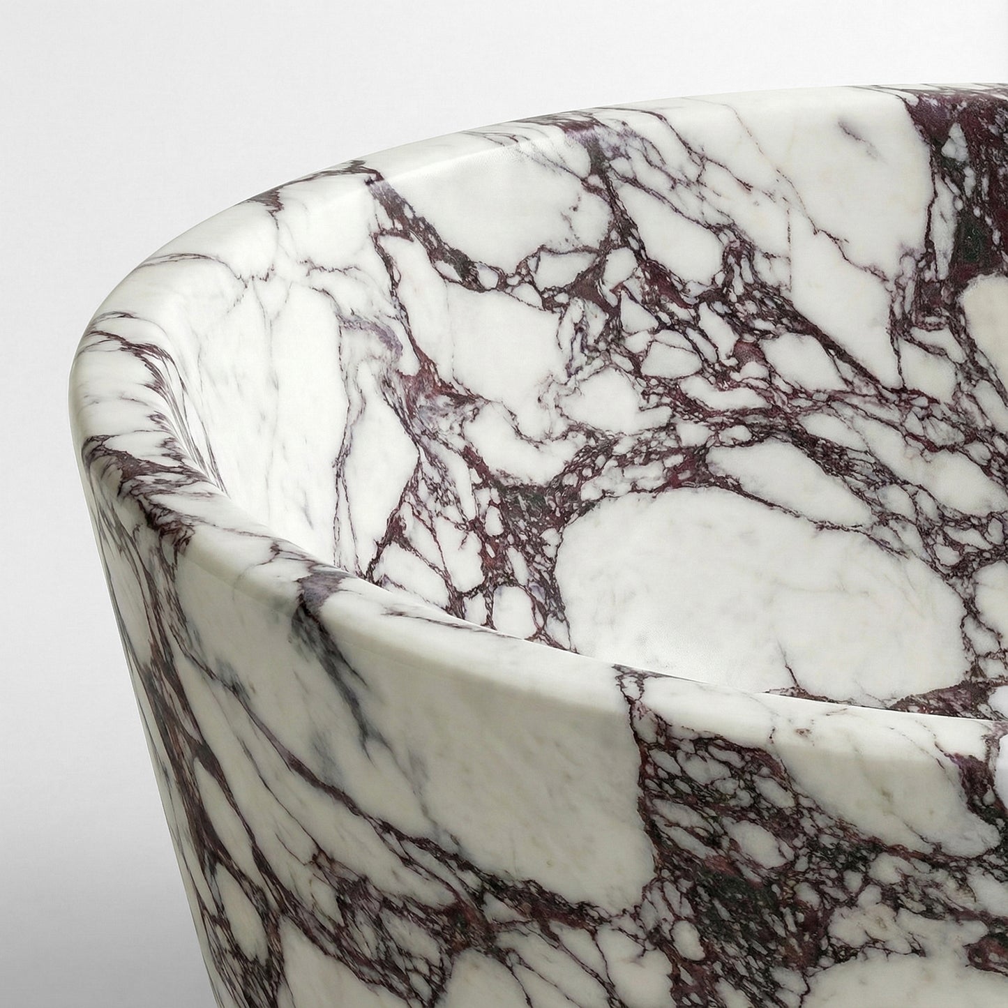Close-up detail of a Calacatta Viola marble bathtub rim showcasing deep burgundy veining on a polished white natural stone surface.