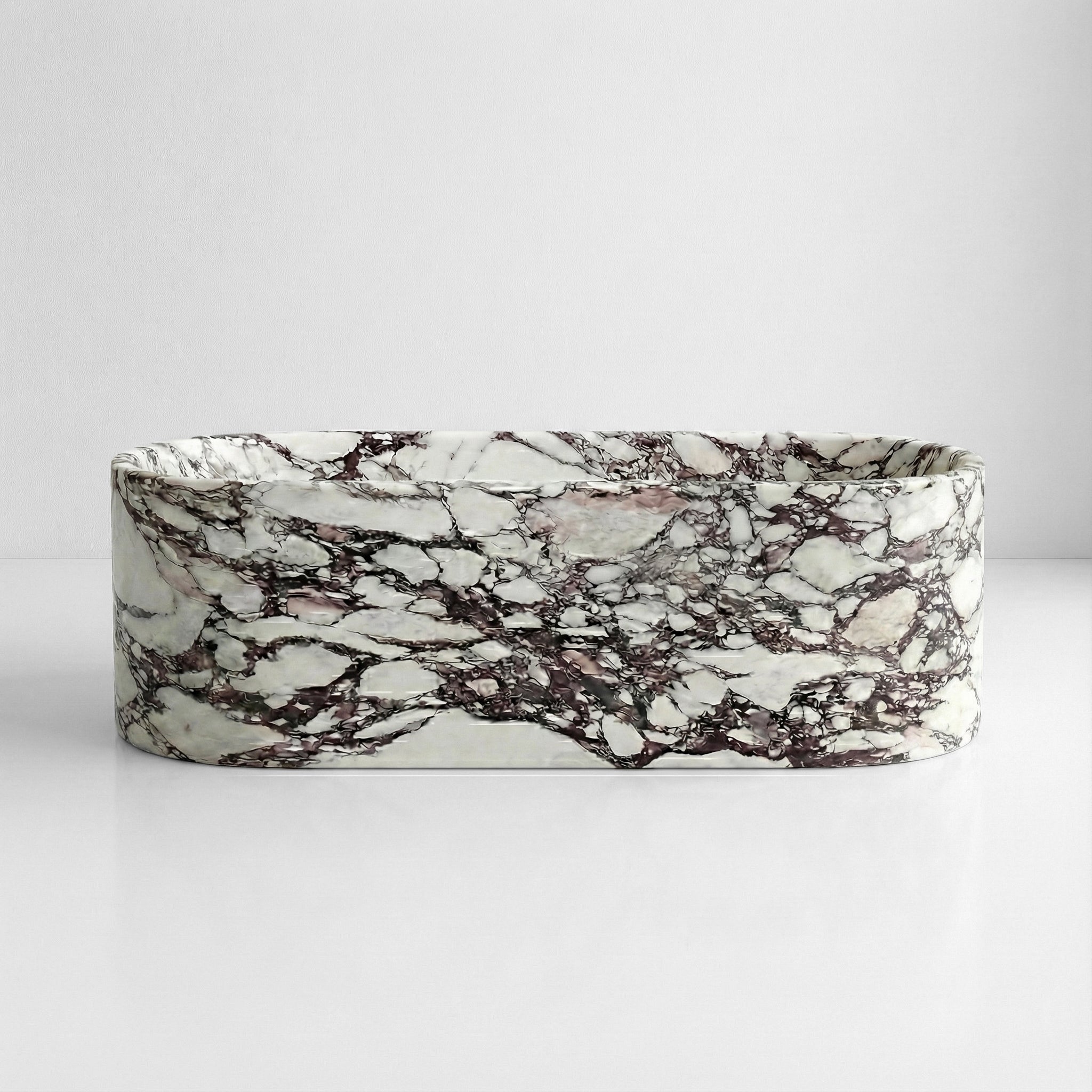 Front view of a freestanding oval bathtub made from polished Calacatta Viola marble with dramatic purple veining.