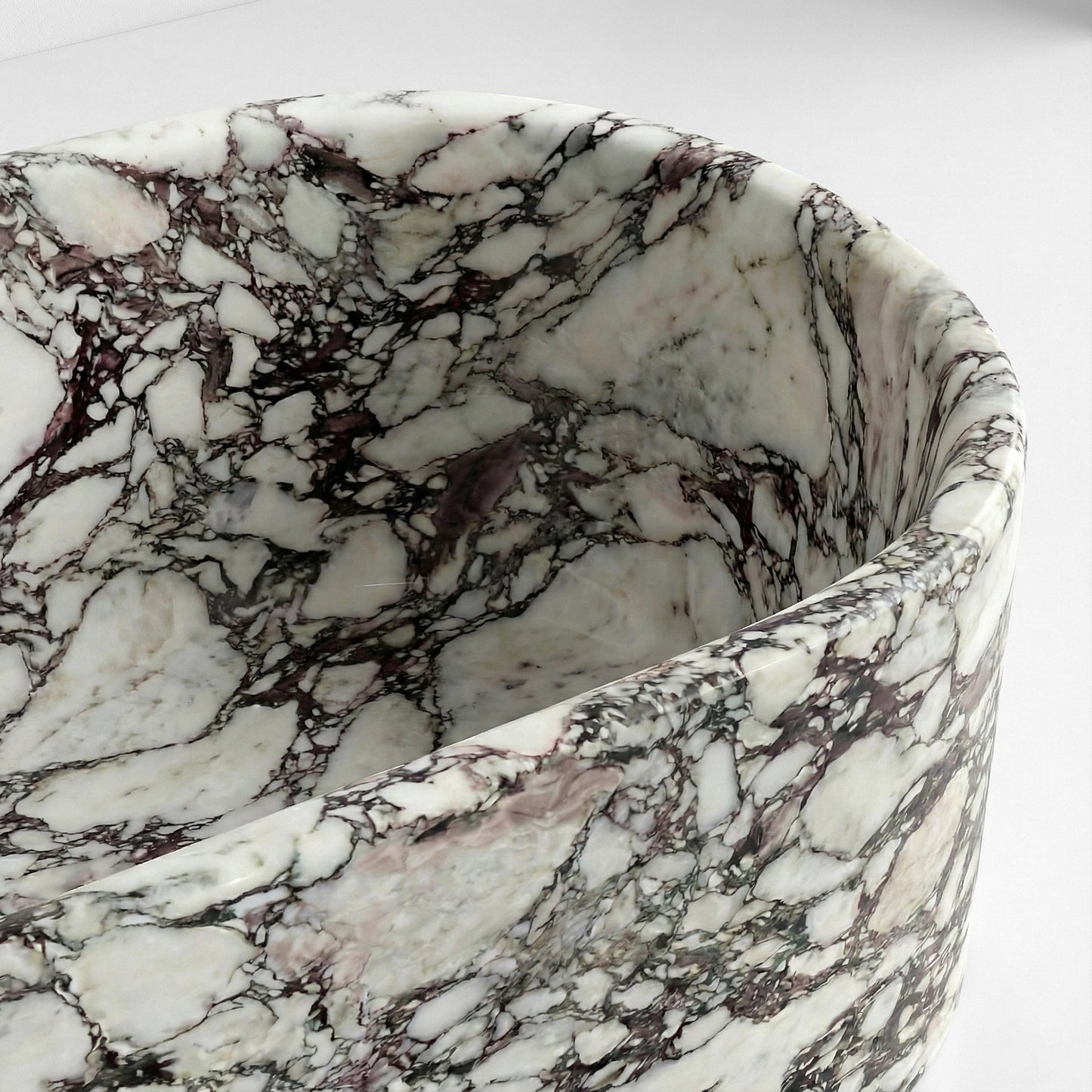 Close-up detail of Calacatta Viola marble bathtub rim featuring deep burgundy and white brecciated veining.