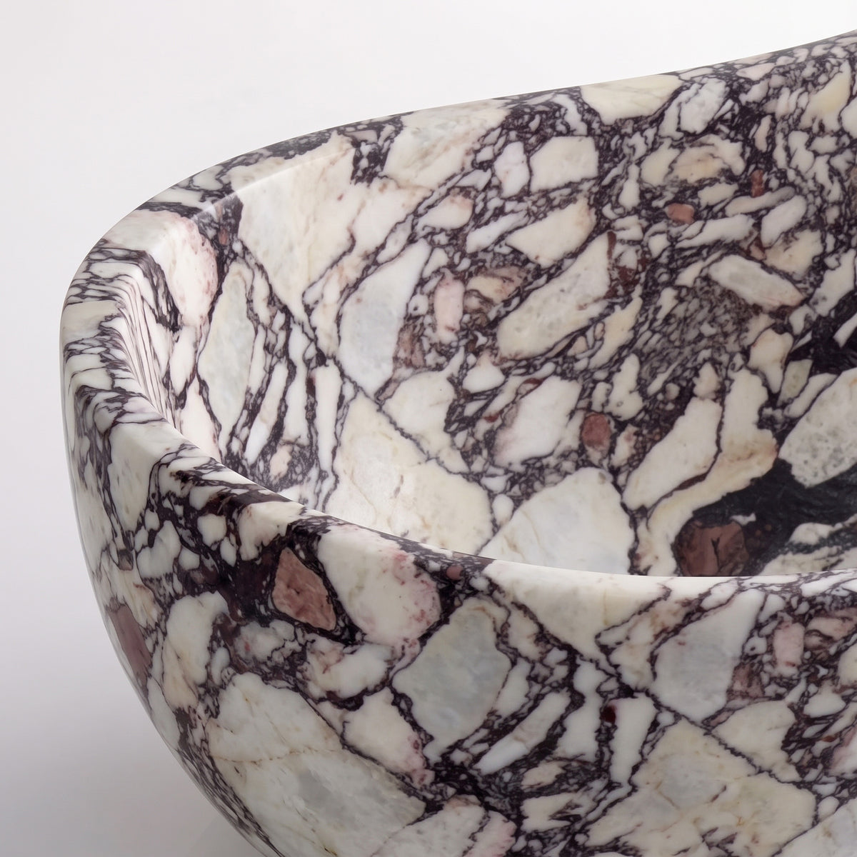 Close-up overhead detail shot of the Calacatta Viola marble wave bathtub rim, displaying the hand-finished curve, smooth stone surface, and high-contrast violet-burgundy breccia fragments on crystalline white Italian marble