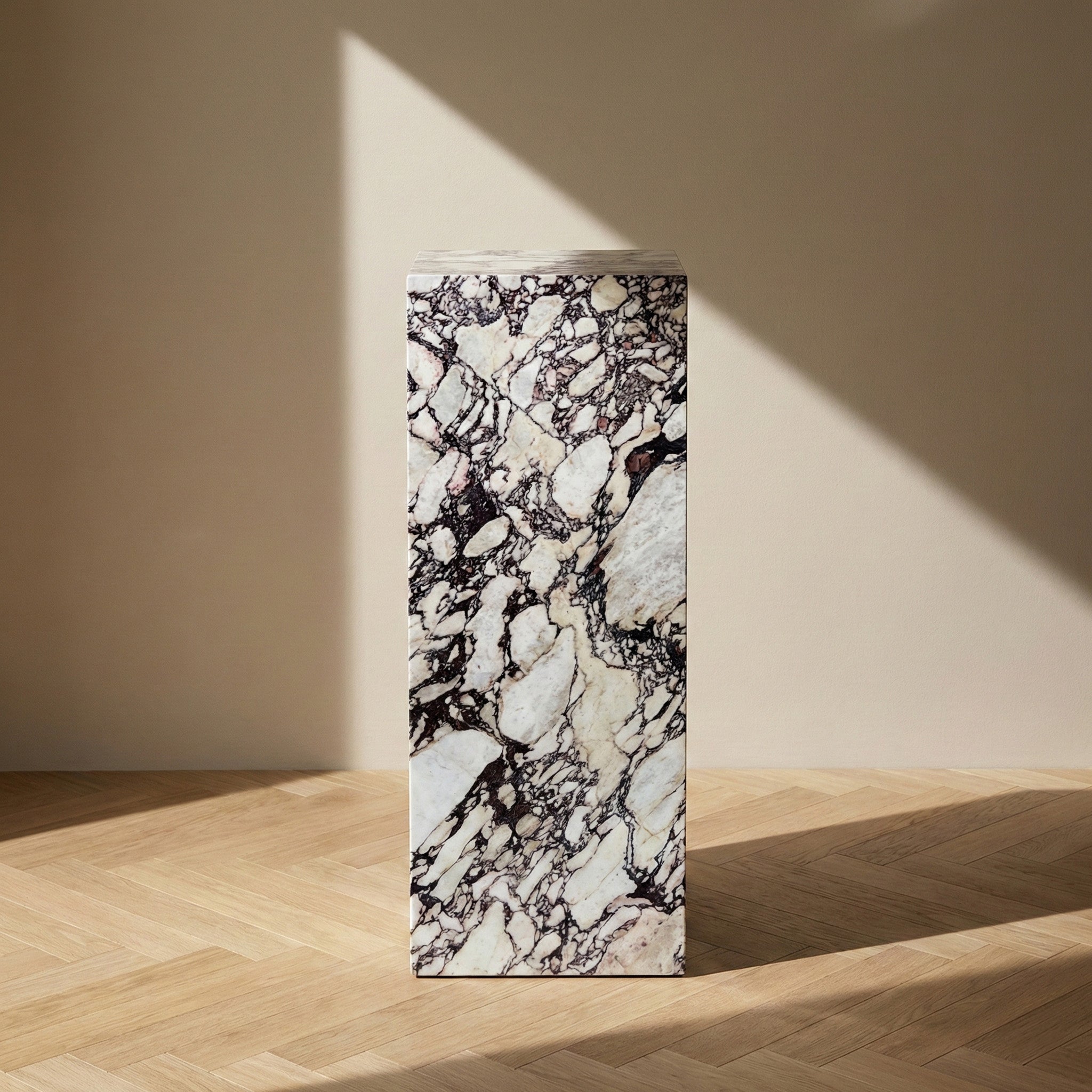 A direct, front-facing view of a Calacatta Viola marble pedestal stand against a neutral wall, showing the striking vertical contrast of the dark wine-colored veins against the white stone background.