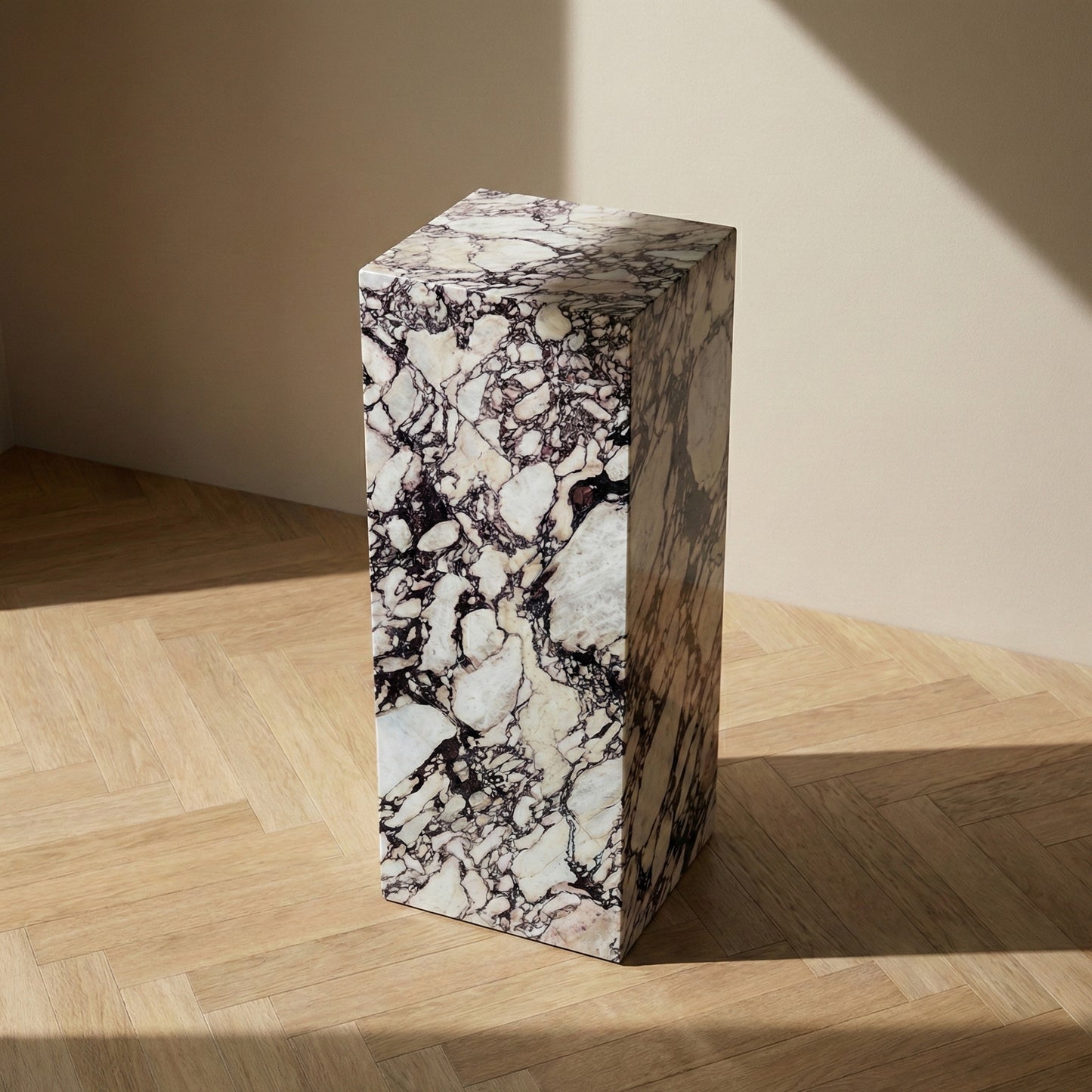 An angled perspective view of a rectangular Calacatta Viola marble plinth standing on a light wood herringbone floor, highlighting its three-dimensional form and rich veining.